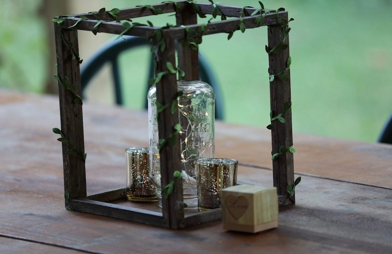 Rustic wooden frame centerpiece with glass jar candles and green vine accents on a wooden table.