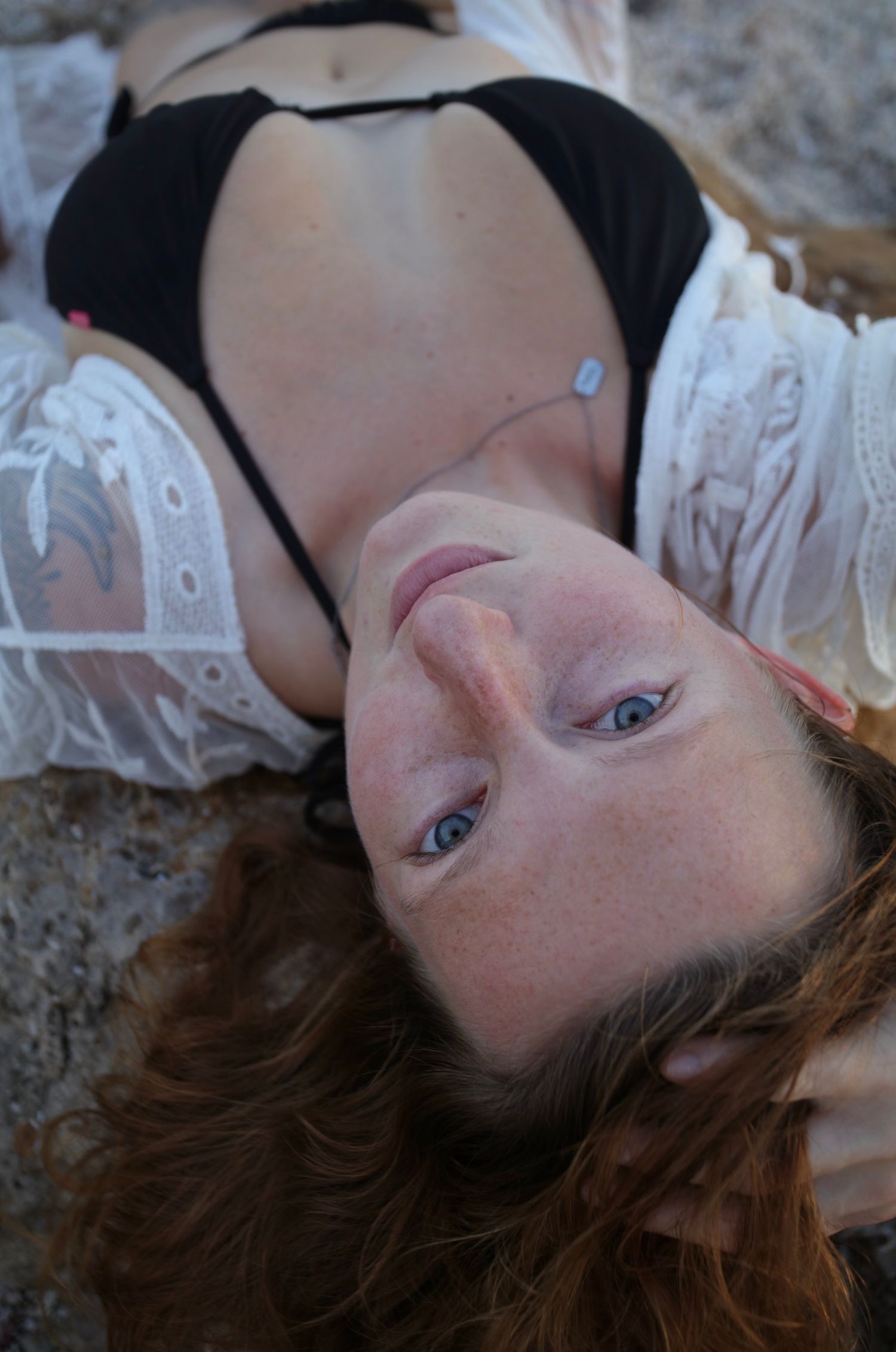 Close-up overhead view of blue-eyed woman in black bikini lying on sandy beach.