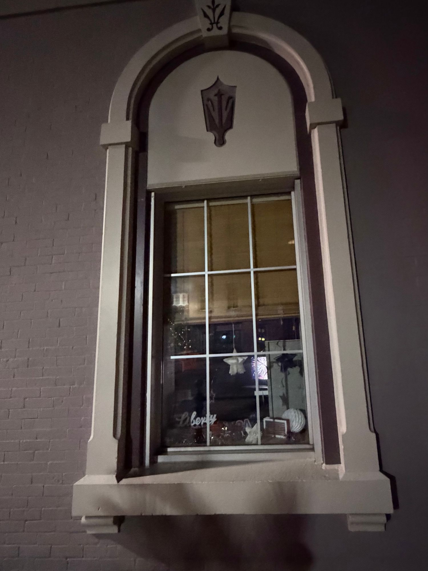 Elegant arched window with decorative molding and keystone detail on a white brick wall at night.