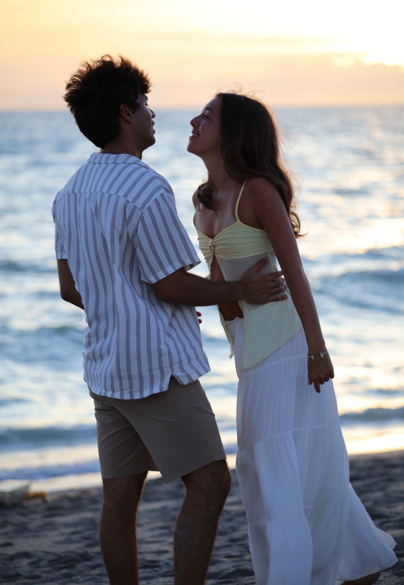 Happy couple embracing and gazing at each other on a sandy beach at golden sunset.