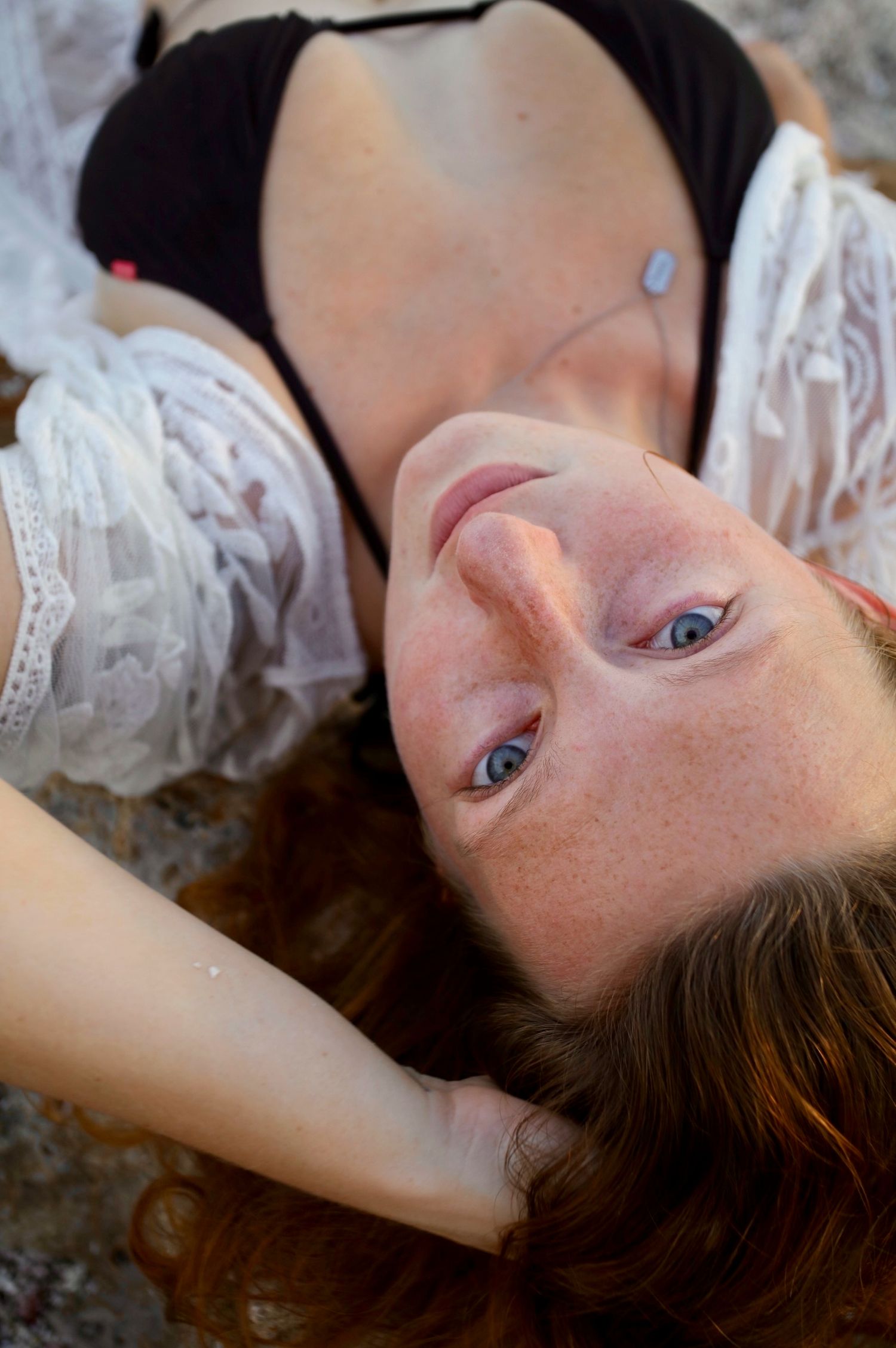 Close-up of a freckled redhead woman with blue eyes lying on rocks wearing a black bikini top.
