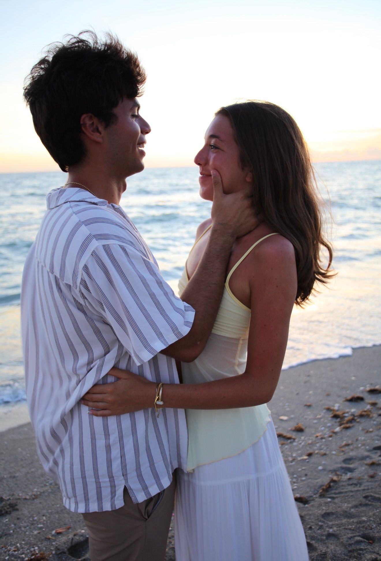 Young couple gazing at each other romantically on beach at golden sunset by the ocean.