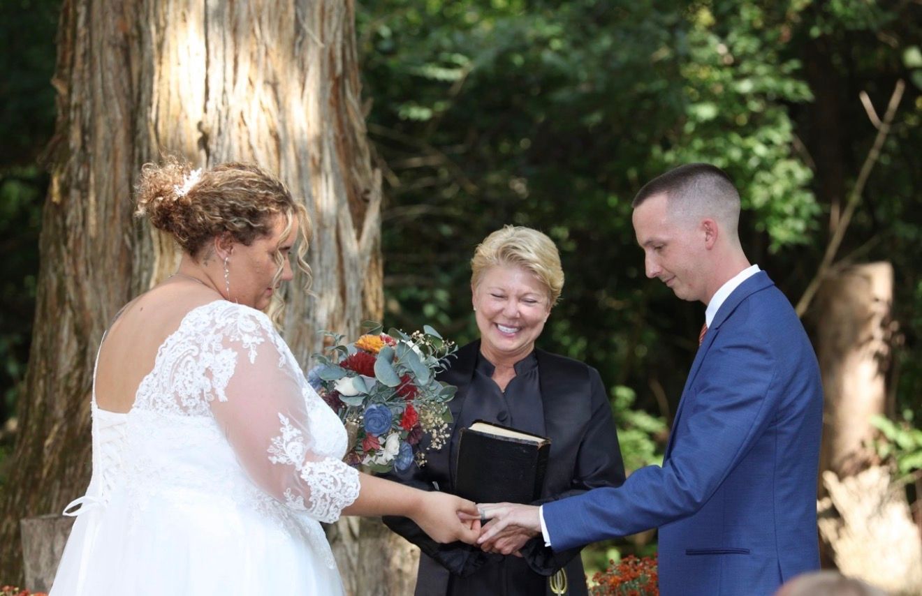 Bride and groom exchange vows with officiant outdoors among tall redwood trees during intimate wedding ceremony.