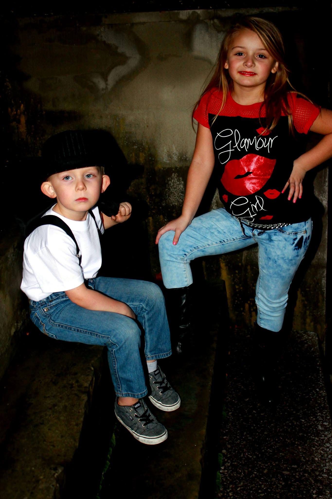 Two children in jeans pose on steps, boy in white shirt and black hat, girl in red Glamour Girl top.