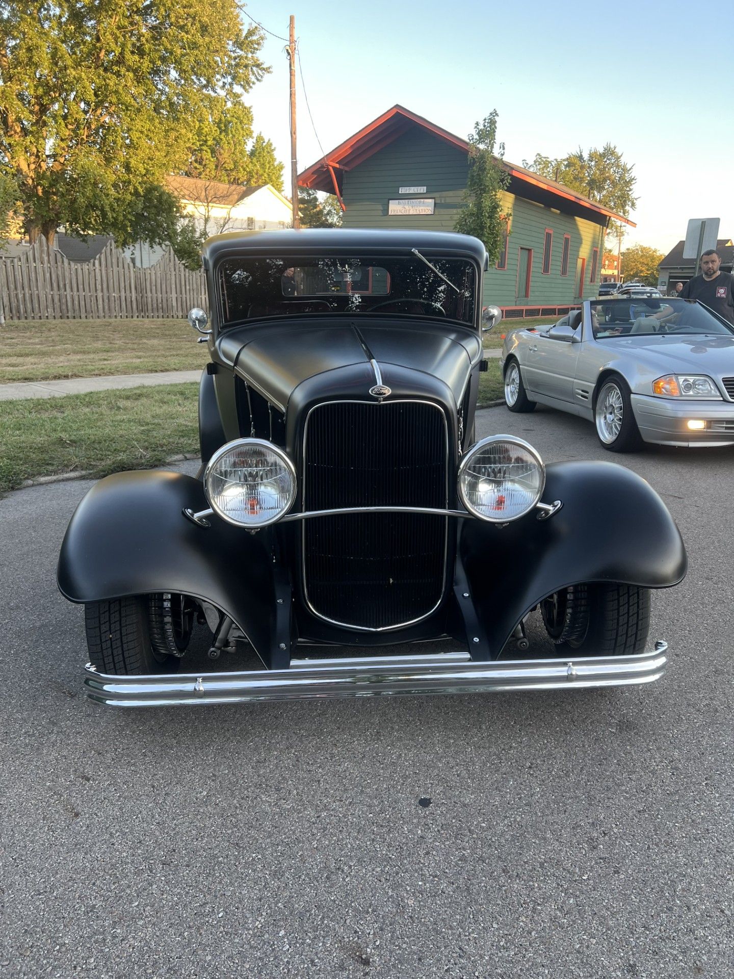 Vintage black hot rod classic car with chrome headlights parked on a street, featuring a matte finish and retro styling.