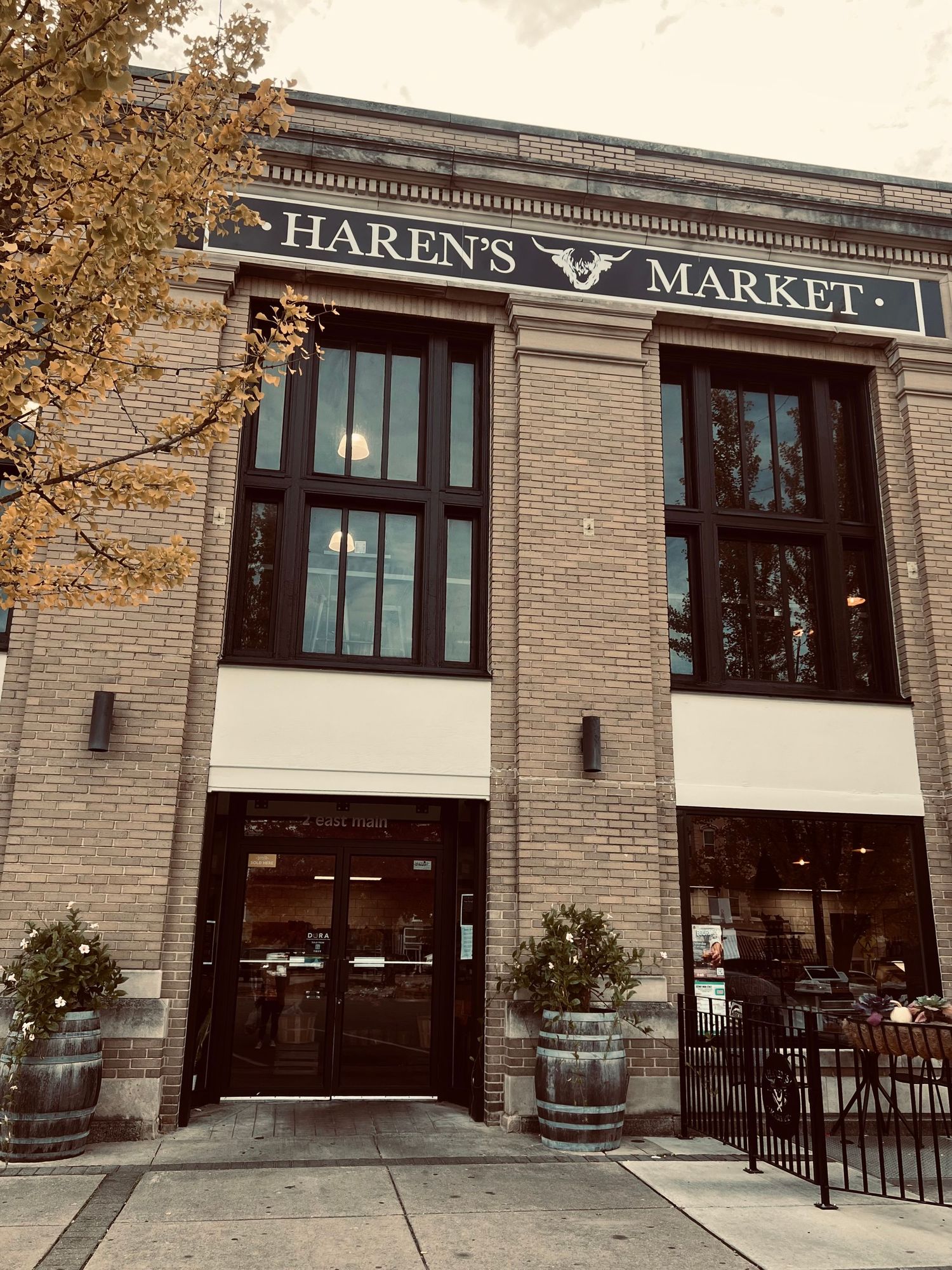 Haren's Market brick building exterior with large windows, barrel planters, and signage in a charming urban setting.
