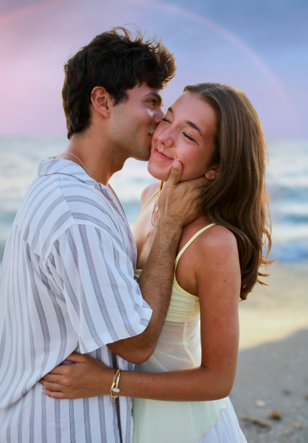 Couple sharing a romantic kiss on the beach at sunset, man gently holding woman's face.
