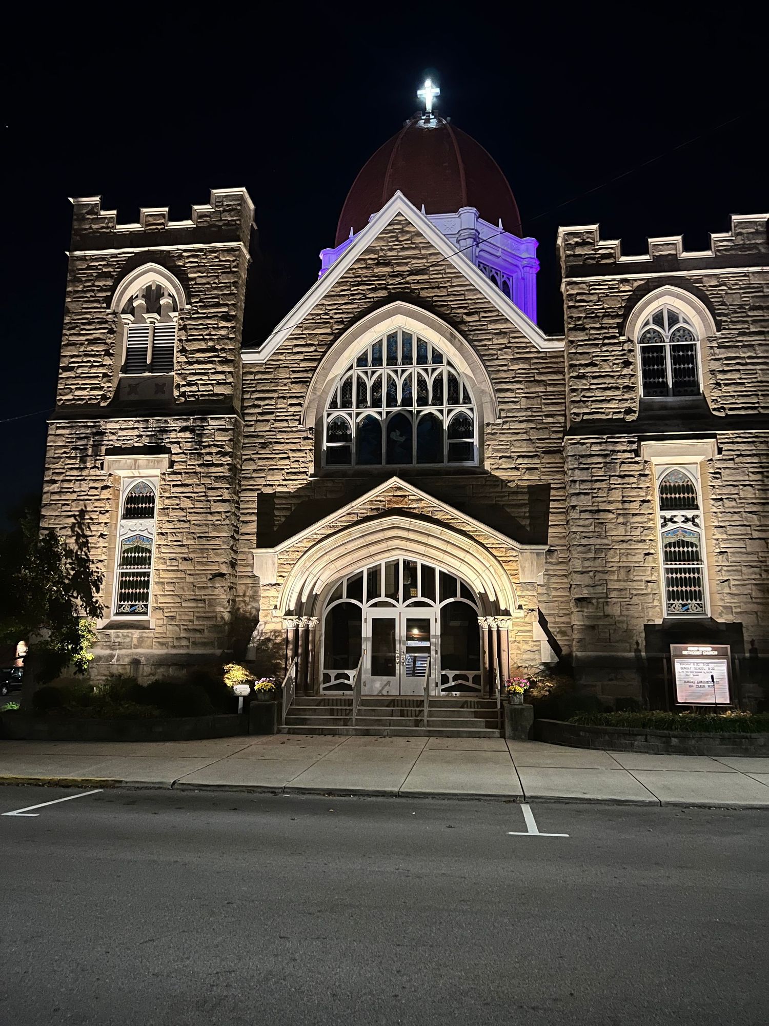 Historic stone church illuminated at night with purple dome and cross atop the entrance.