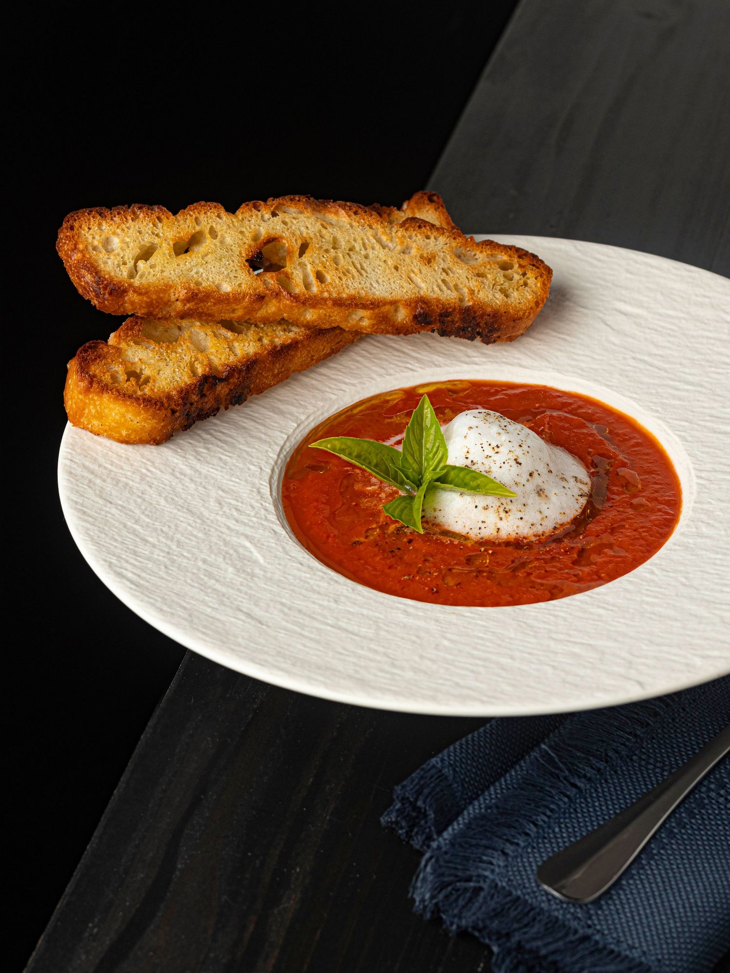 Tomato soup in a large white bowl with crostini on a black background