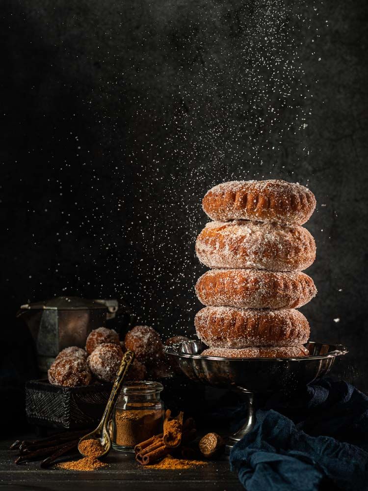 Front view of a stack of spiced donuts with powdered sigar falling from above on a blue background