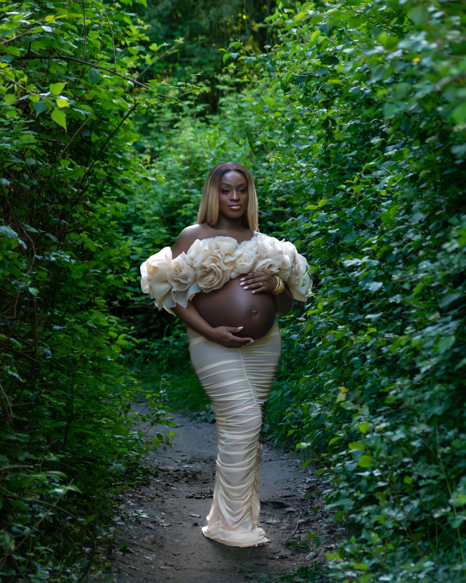 Femme enceinte en robe fleurie blanche, séance photo dans un chemin verdoyant