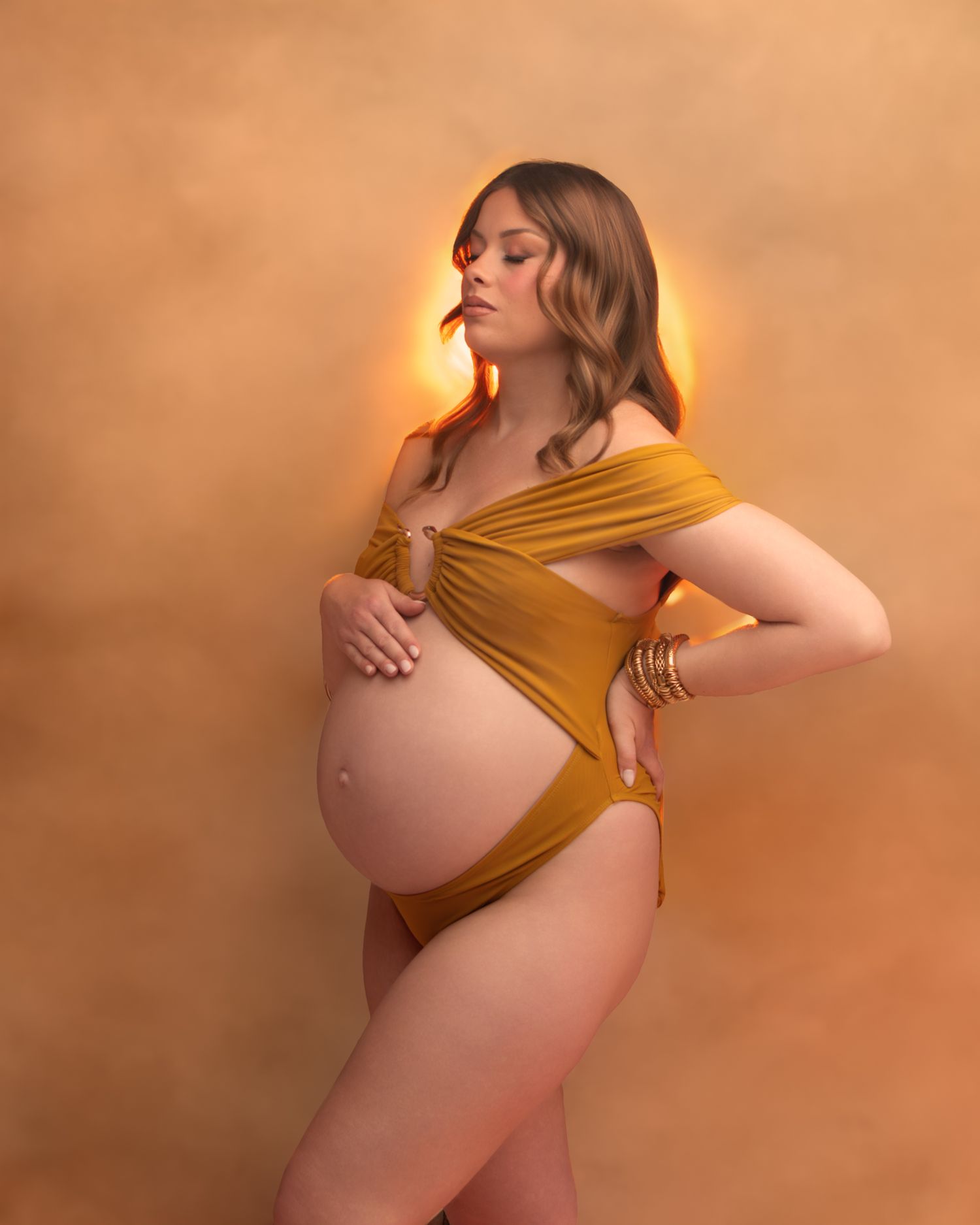 Photo de grossesse en studio, tissu drapé orangé, lumière chaude et dorée