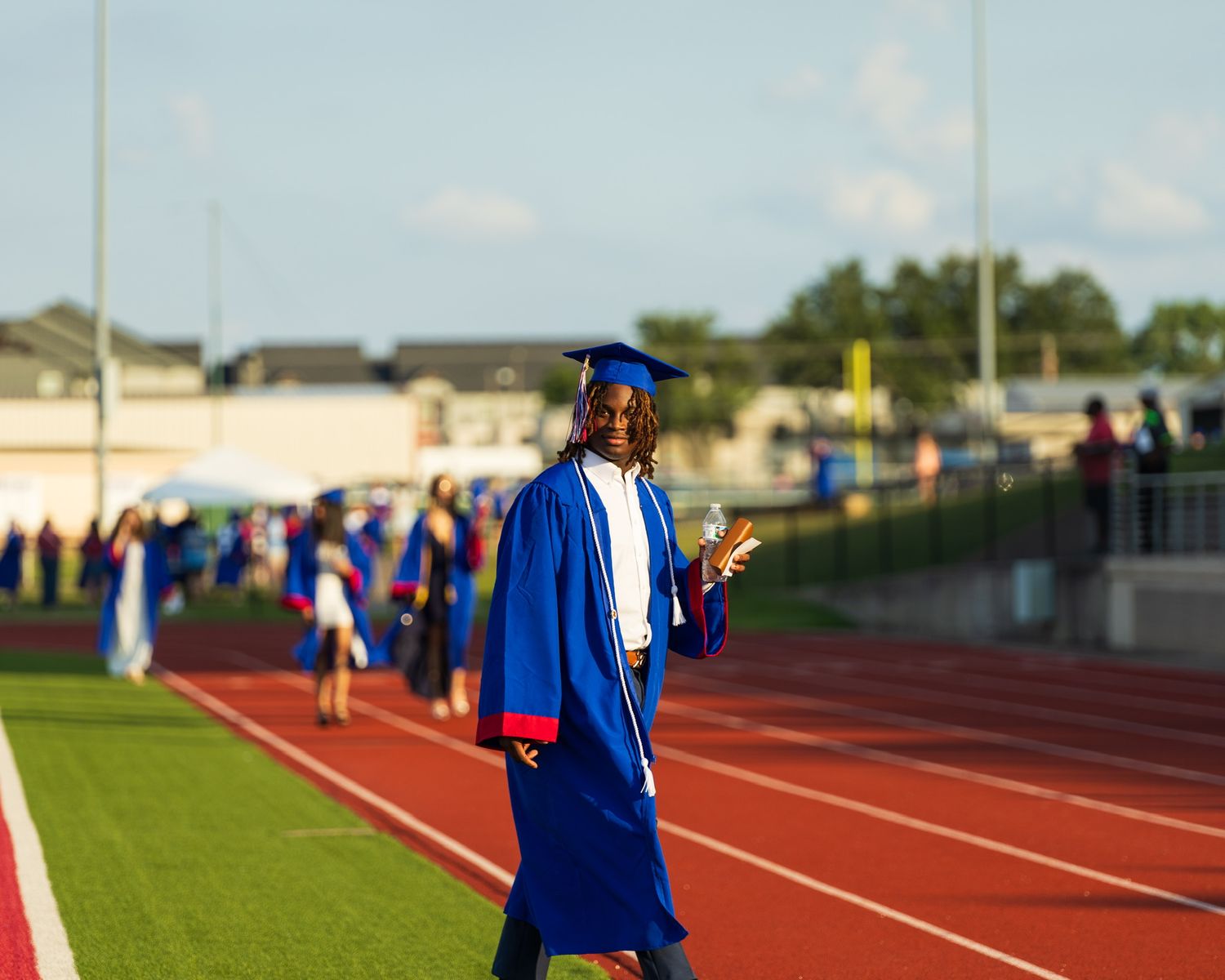 student in cap and gown walking across the football field