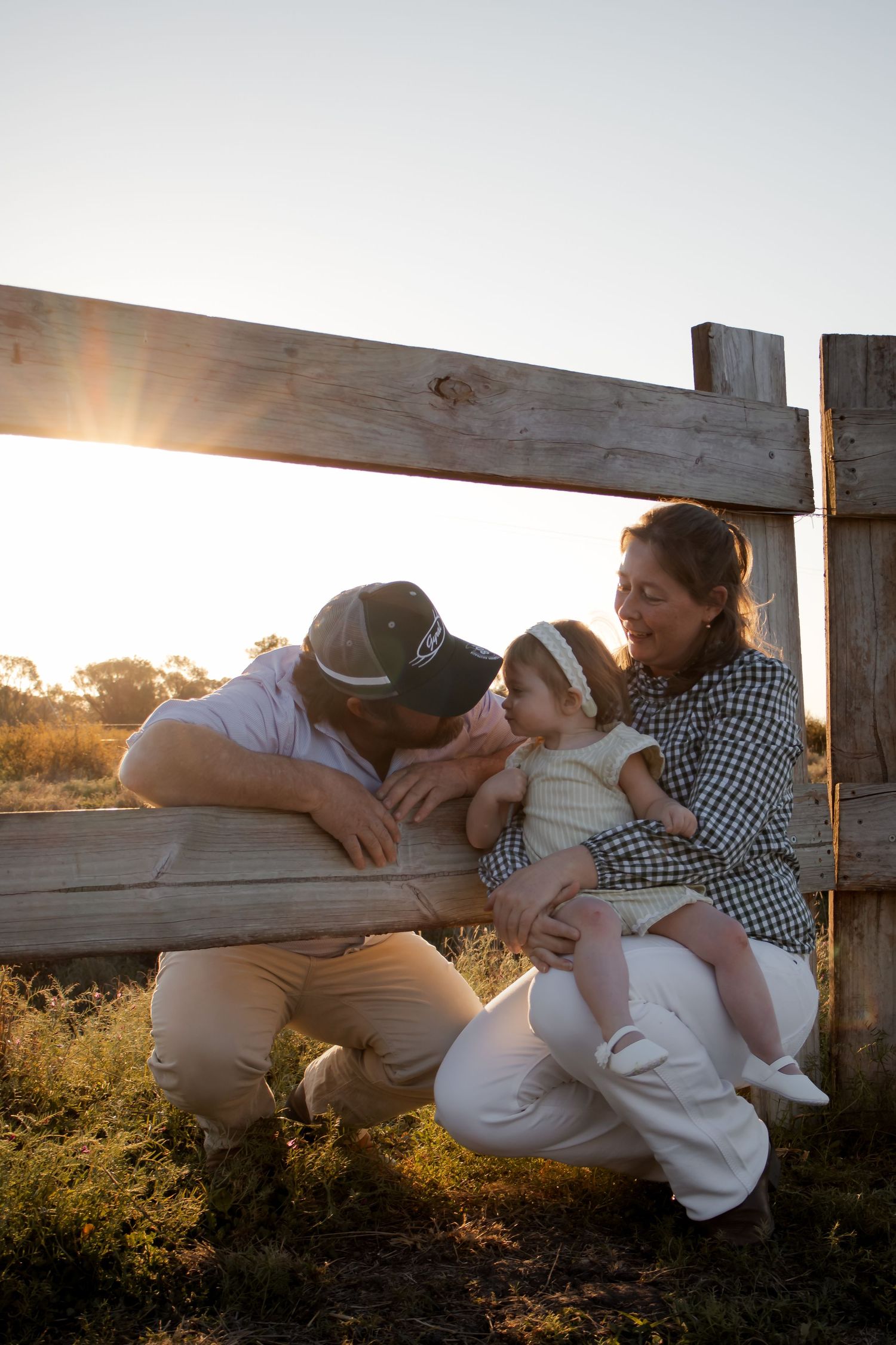 Family sharing a tender moment at sunset by a rustic wooden fence in a golden field.