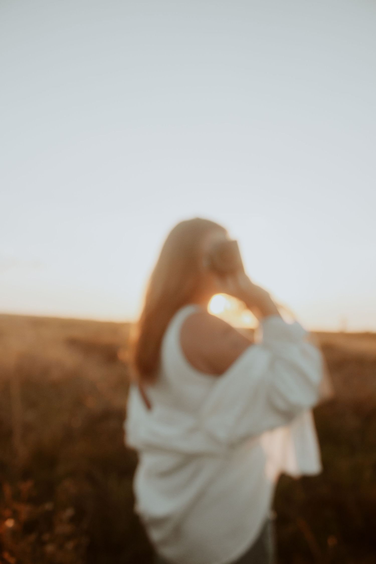 Blurred silhouette of woman with long hair standing in golden sunset field.