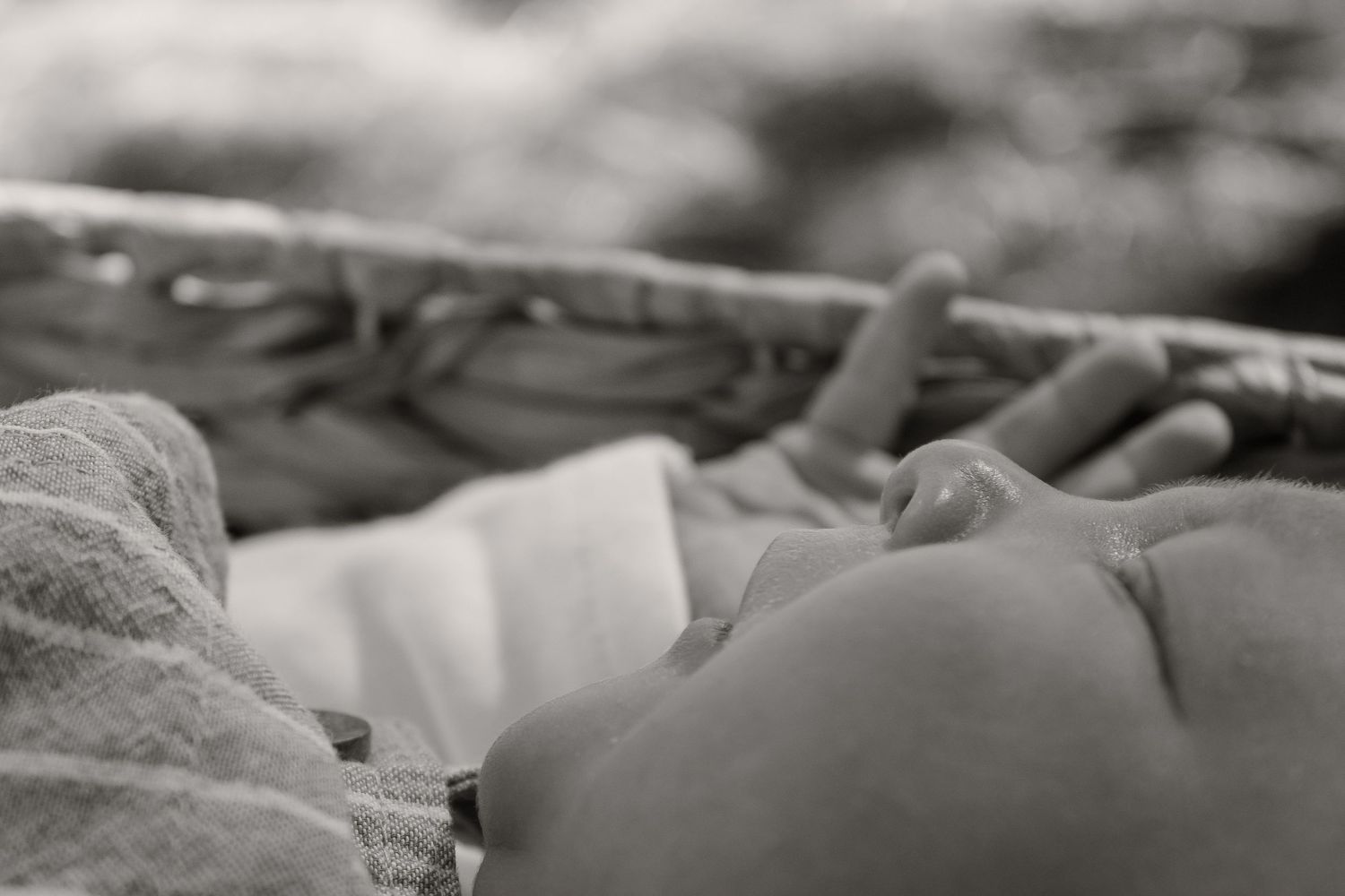 Black and white photo of a sleeping newborn baby resting peacefully in a wicker bassinet.