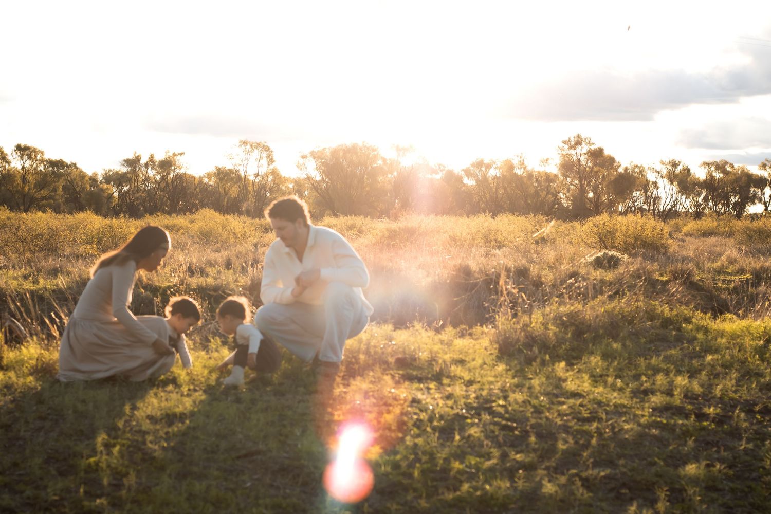 Family enjoying a golden sunset together in a grassy field, bathed in warm sunlight.