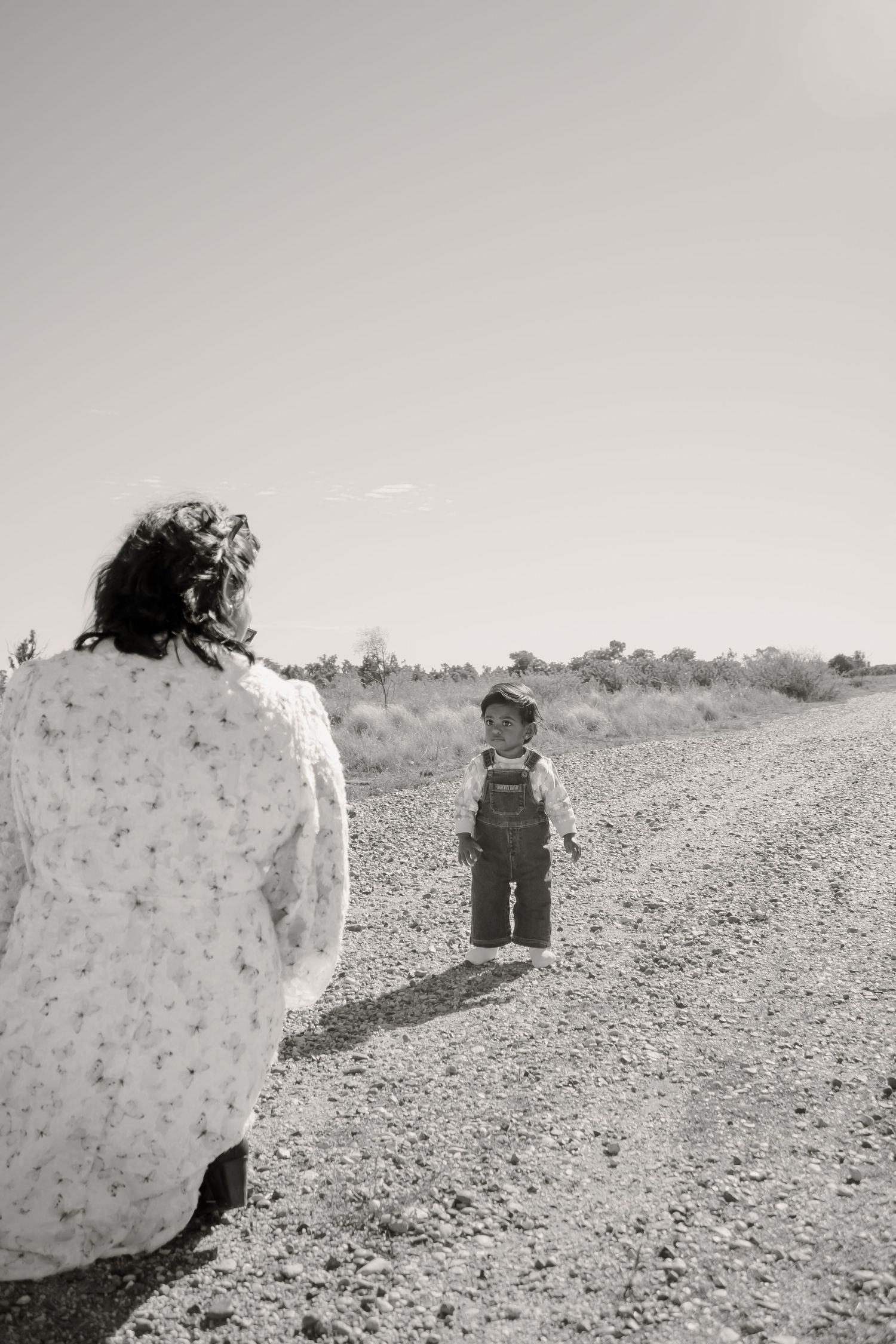 Black and white photo of a woman and toddler standing on a rural dirt road surrounded by open landscape.