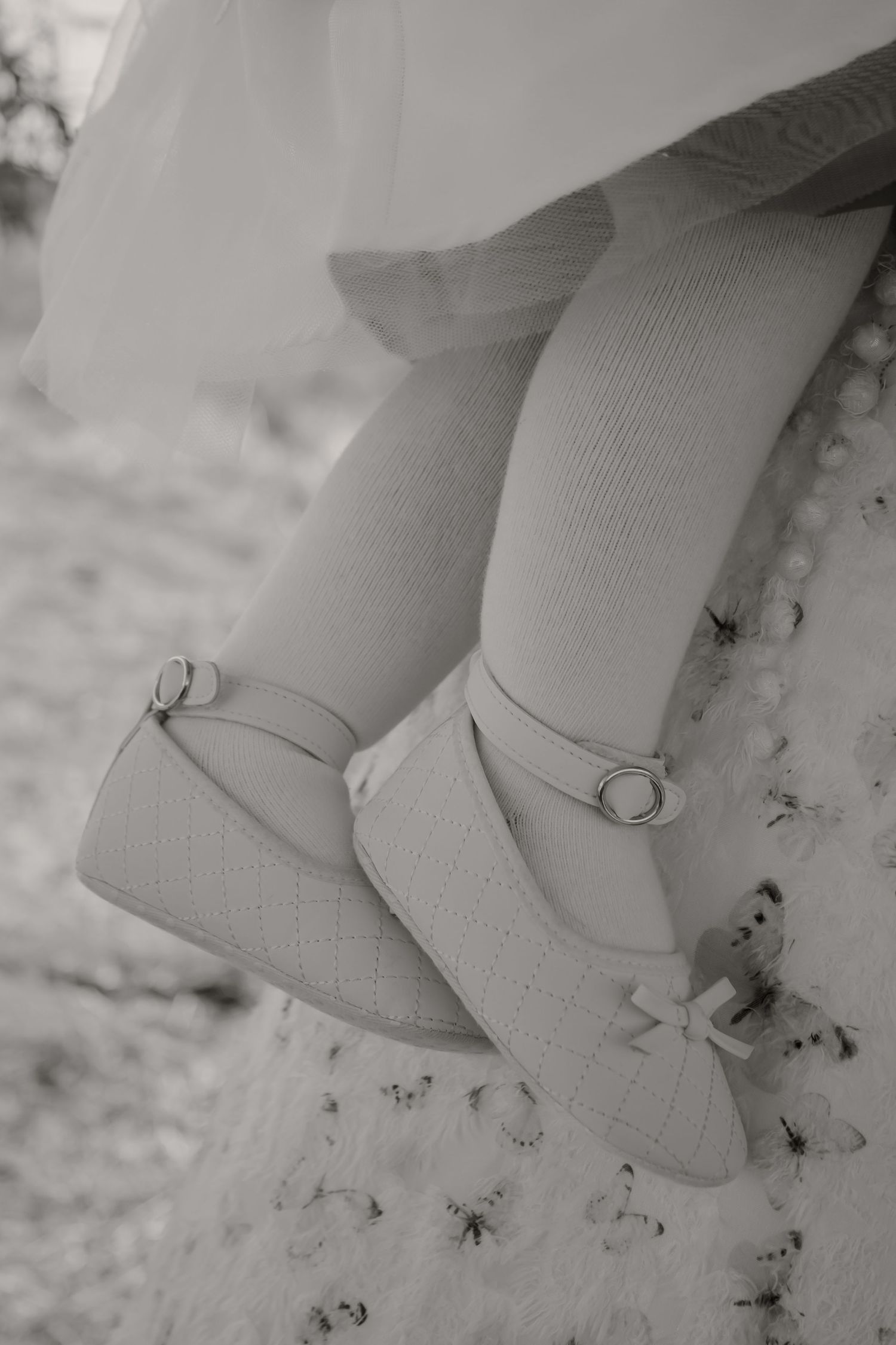 Black and white photo of a little girl wearing white Mary Jane shoes with bows and knee-high socks.