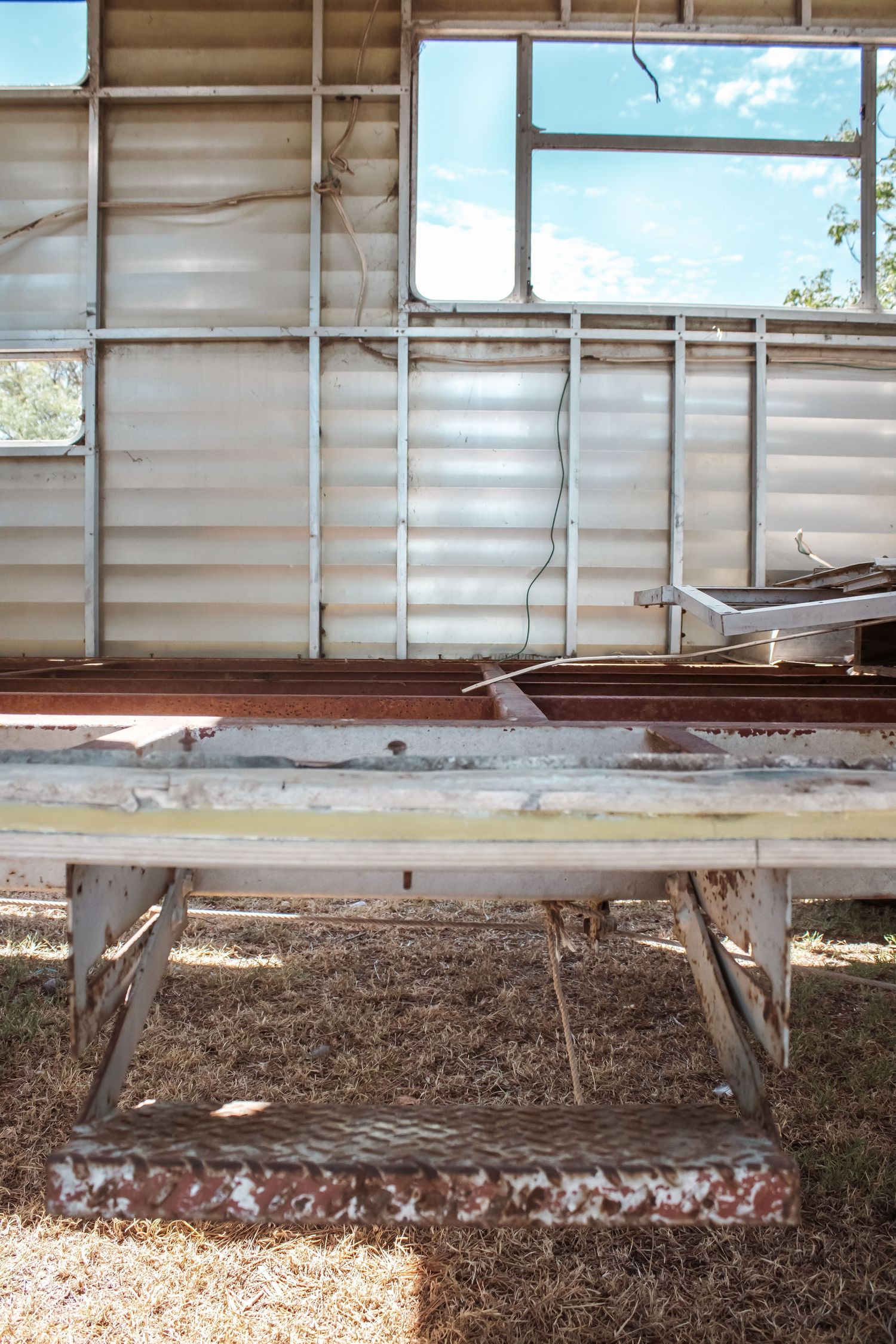 Abandoned rustic building with corrugated metal walls, weathered wooden steps, and rusty beams under a blue sky.