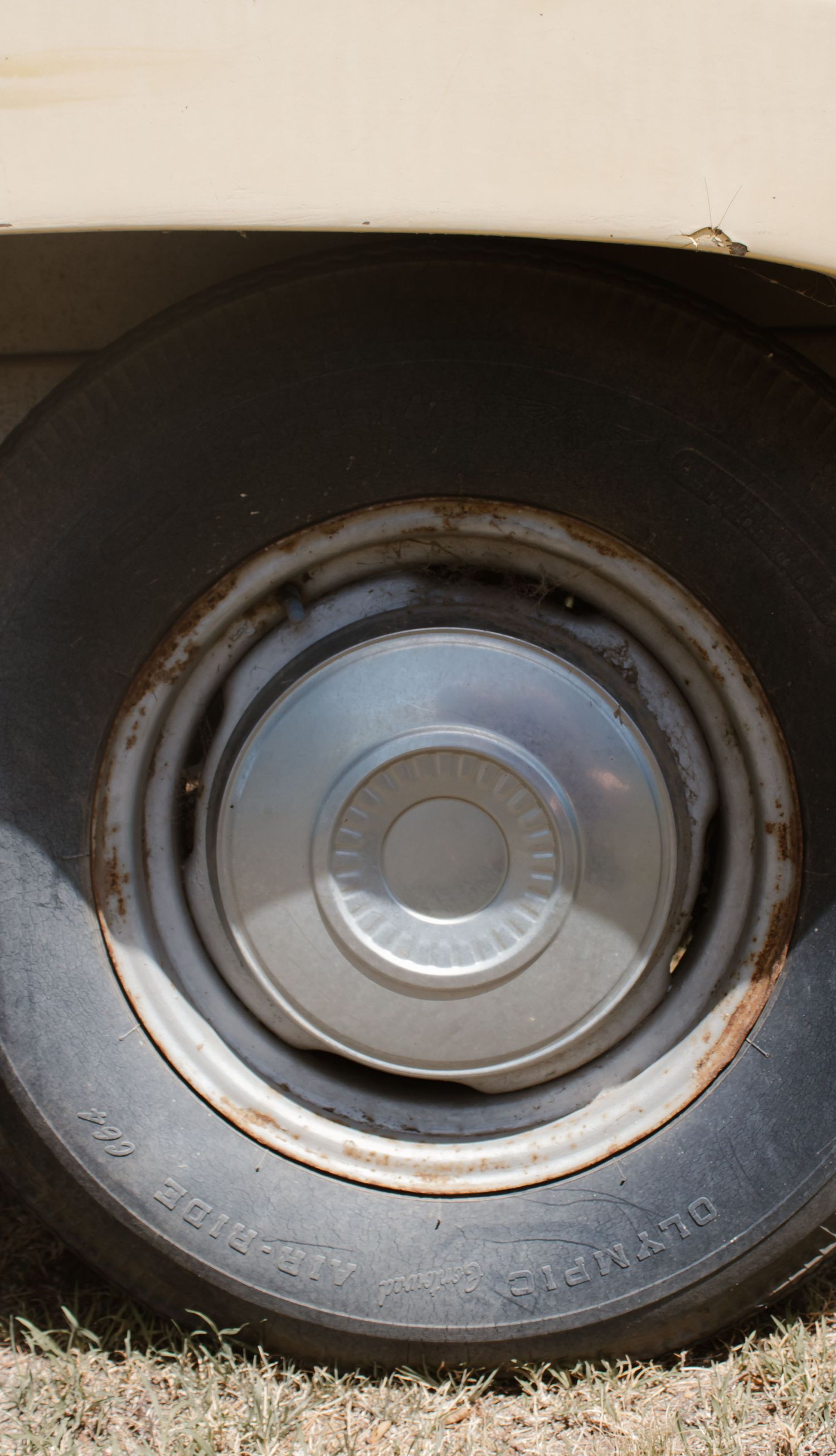 Rusty hubcap on an old Olympia Air-Ride tire on a vintage cream-colored caravan exterior.