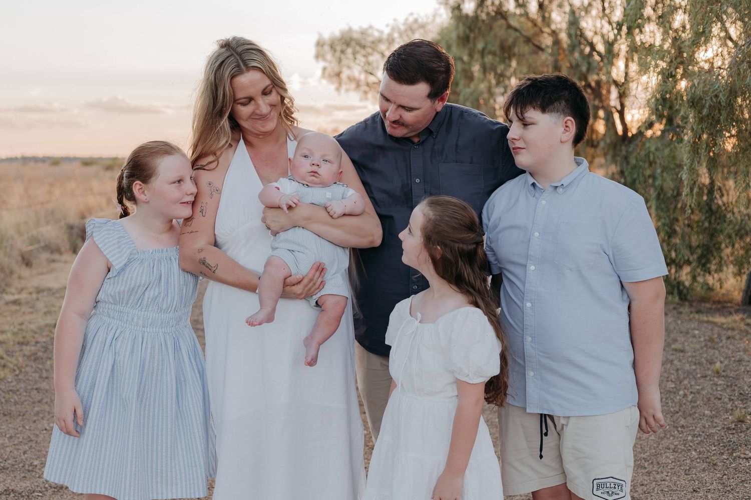 Happy family of six posing outdoors at golden hour in a field, parents holding newborn baby.