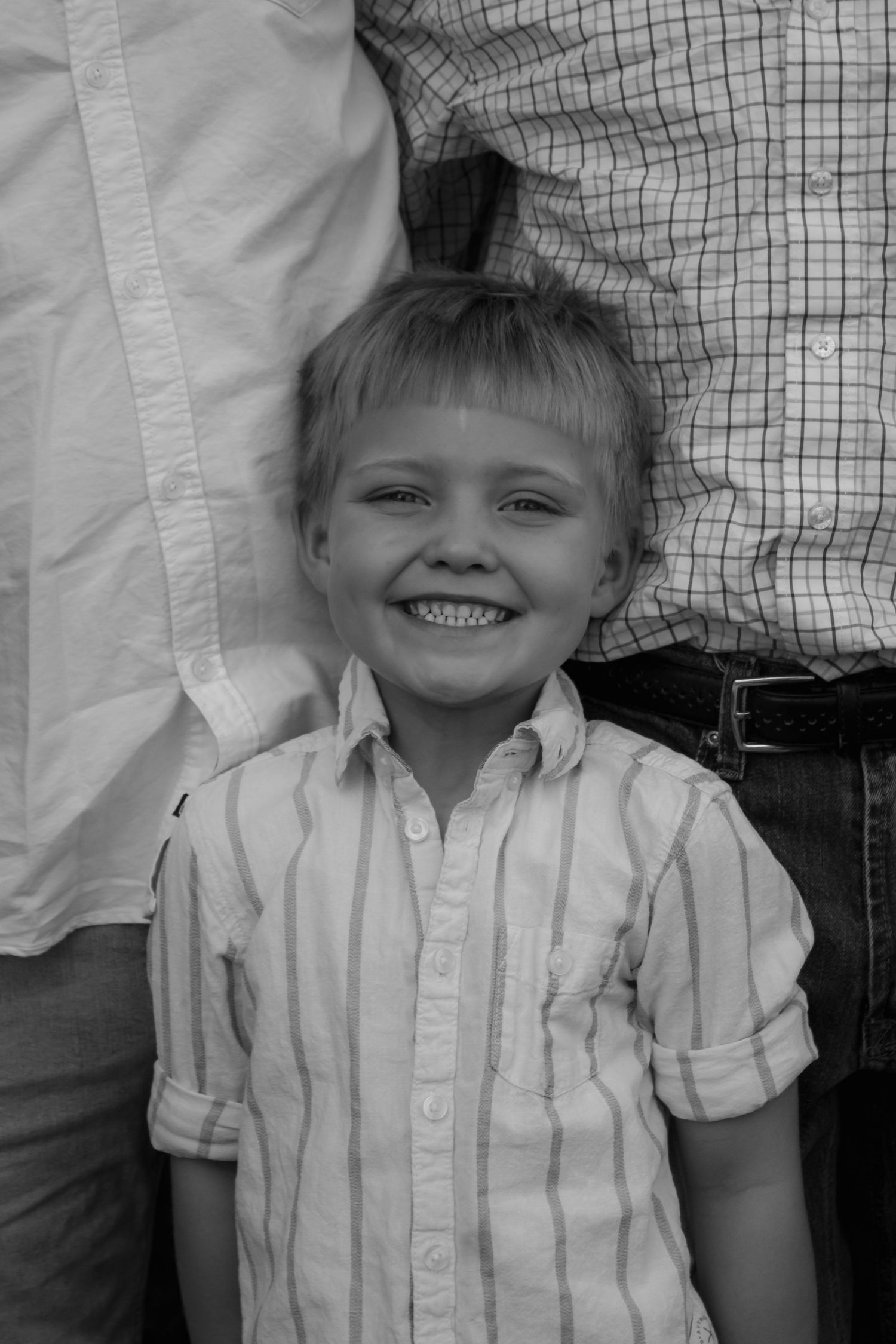 Black and white photo of a smiling young boy in a striped shirt standing between two adults.
