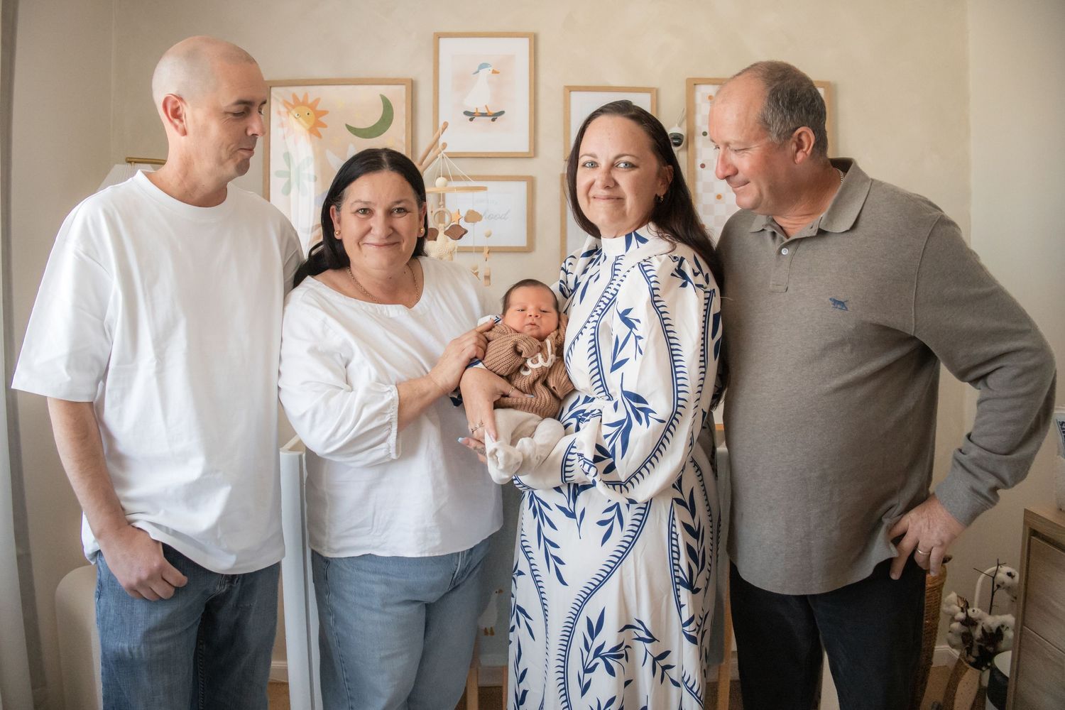 Grandparents standing indoors admiring a newborn baby held by one of the women in a decorated room.