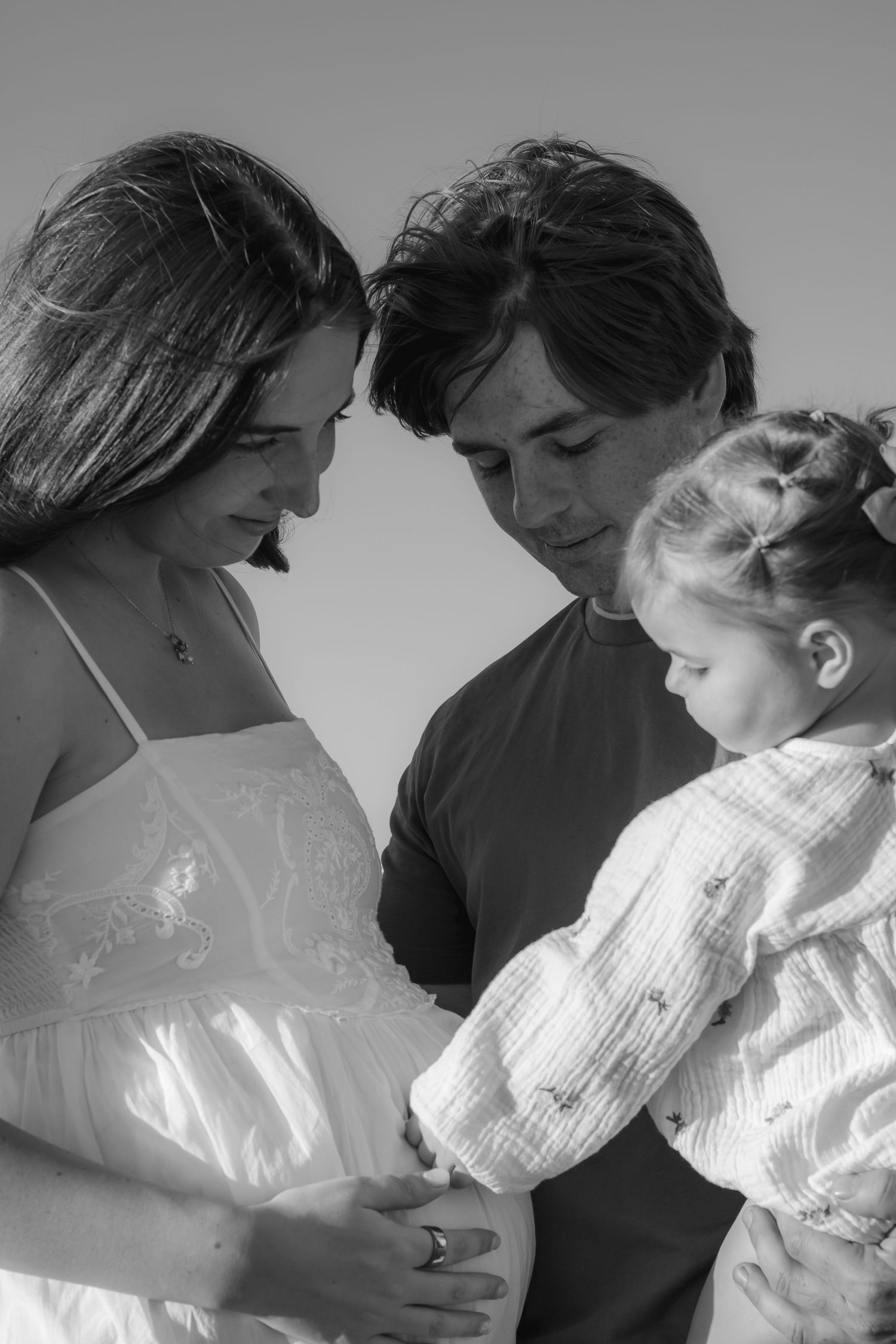 Black and white photo of pregnant woman with husband and young child touching her baby bump.
