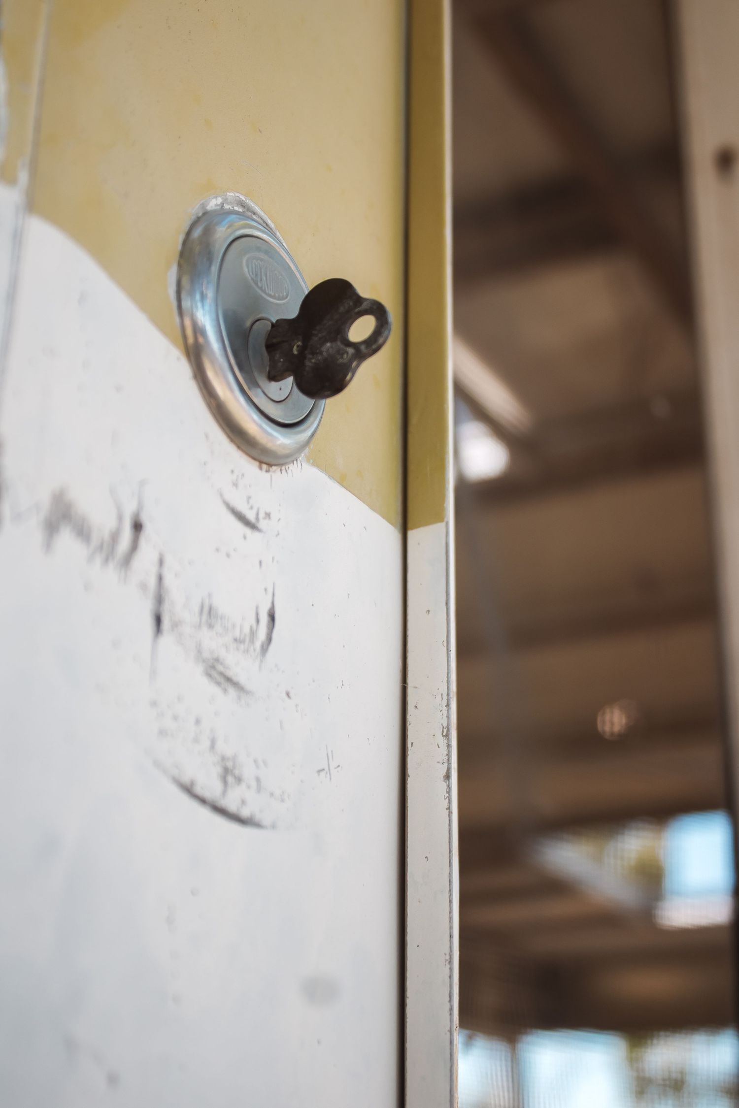 Close-up of a vintage black key inserted in a metal lock on a worn white and yellow wall.
