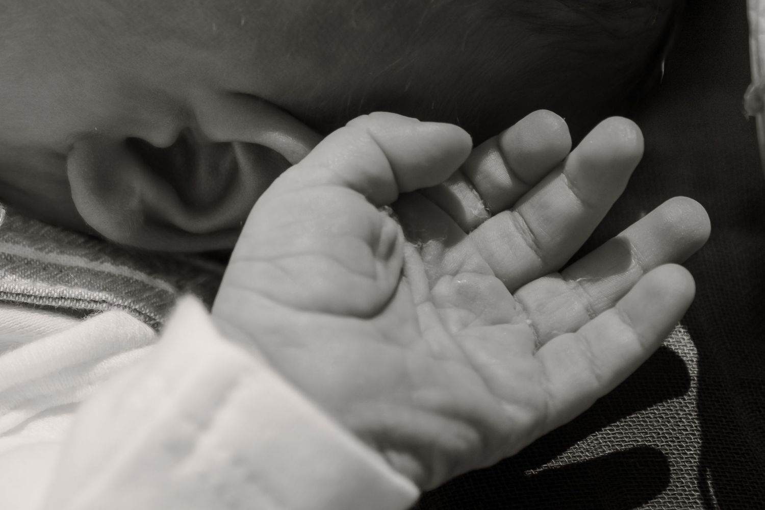 Black and white close-up photo of a newborn baby's tiny open hand next to their ear.
