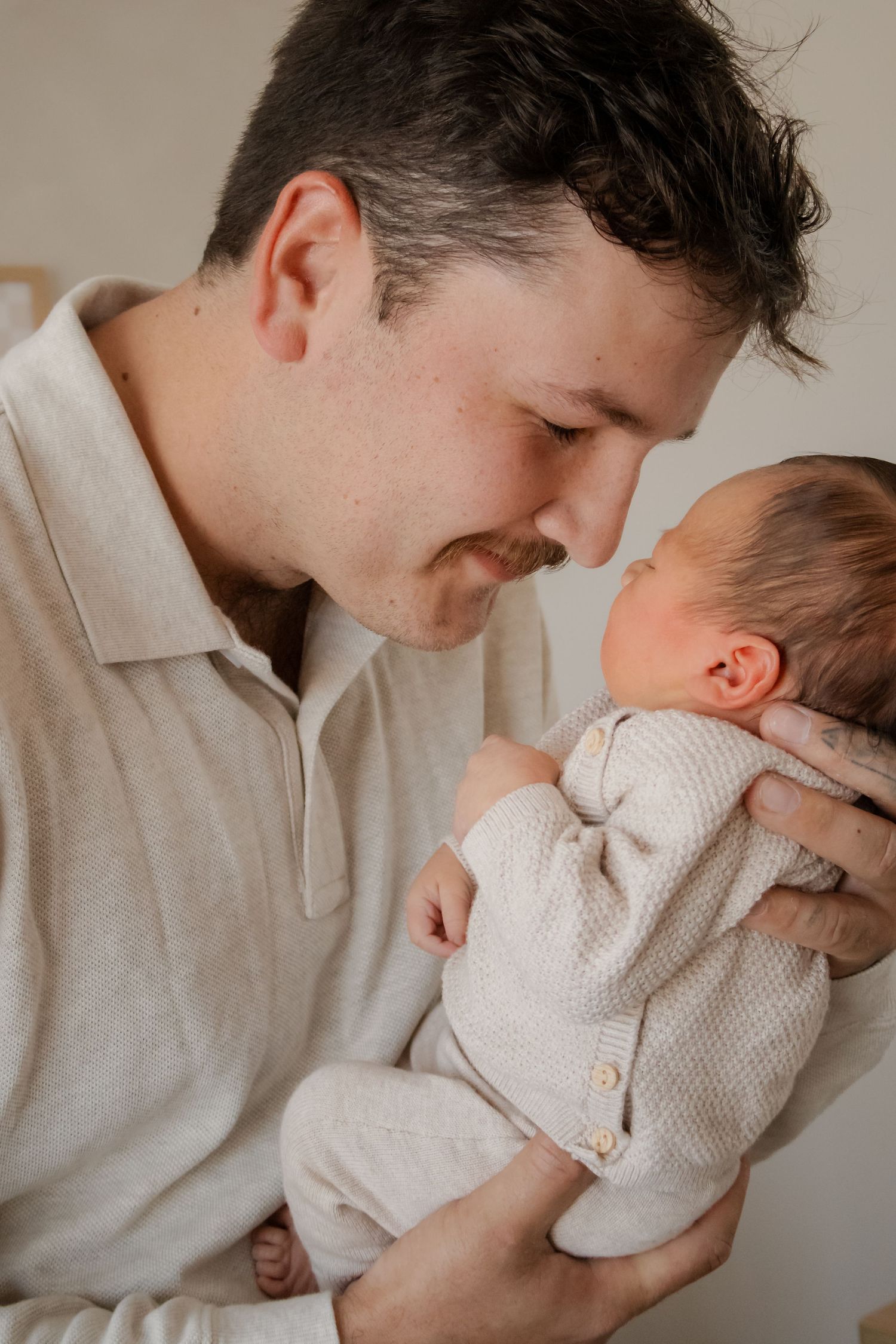 A father tenderly holds his newborn baby close, touching foreheads in an intimate bonding moment.