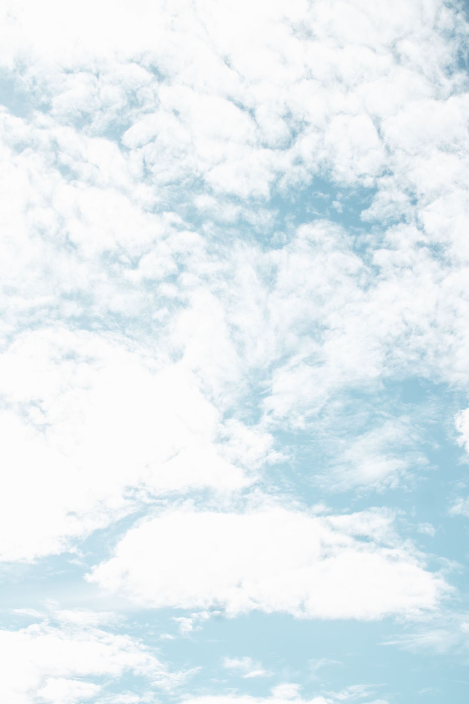 Soft white fluffy clouds scattered across a pale blue sky on a bright clear day.