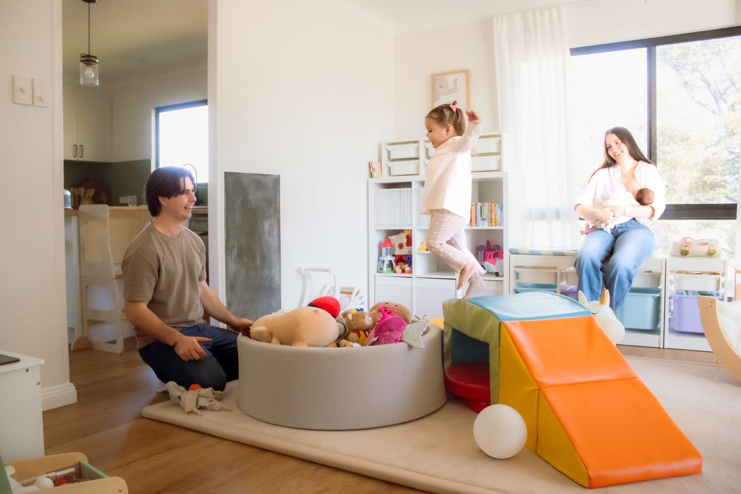 Family enjoying a bright playroom with colorful toys, a ball pit, and a foam slide while parents watch children play.