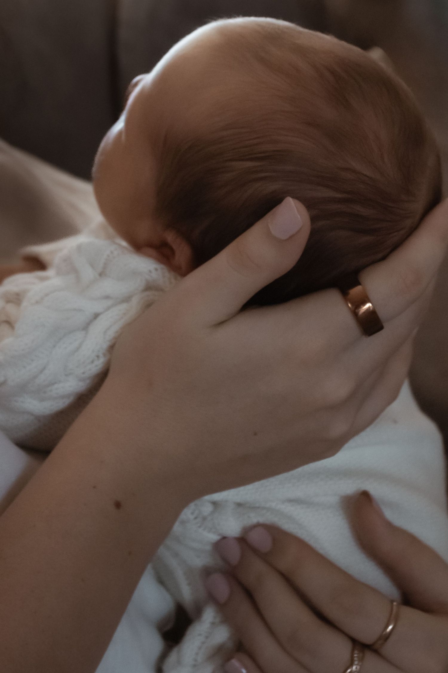 A mother cradling her newborn baby's head with both hands, wearing gold and silver rings.