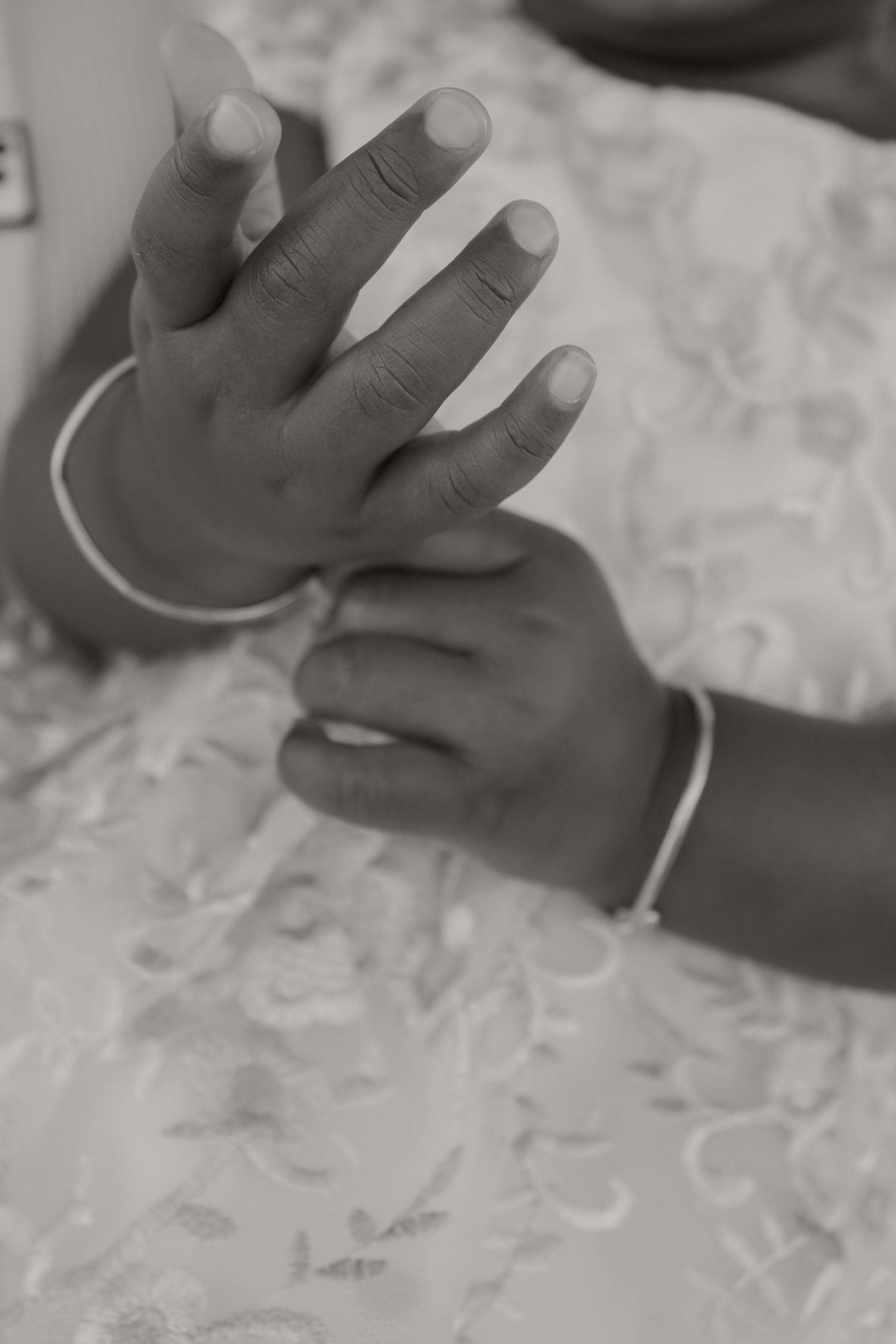Black and white photo of two hands with silver bracelets clasped together on a floral fabric background.