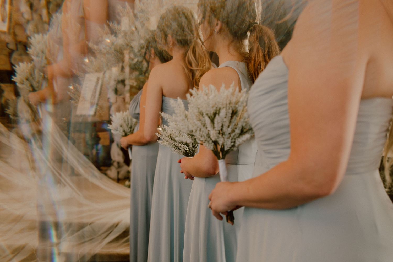 Bridesmaids in light blue gowns hold white floral bouquets during an elegant wedding ceremony.