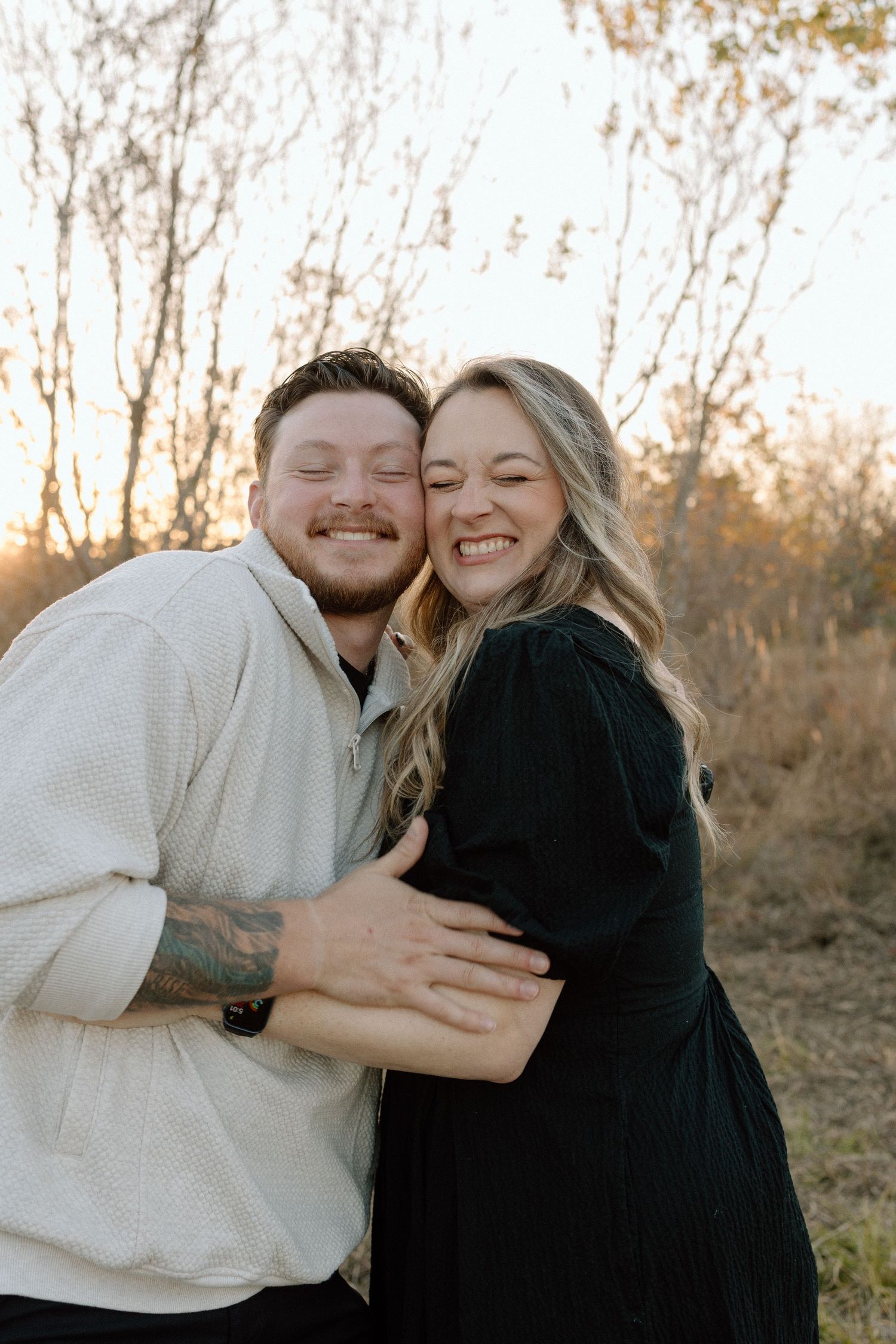 Joyful couple laughs and hugs during a golden sunset engagement photo session.