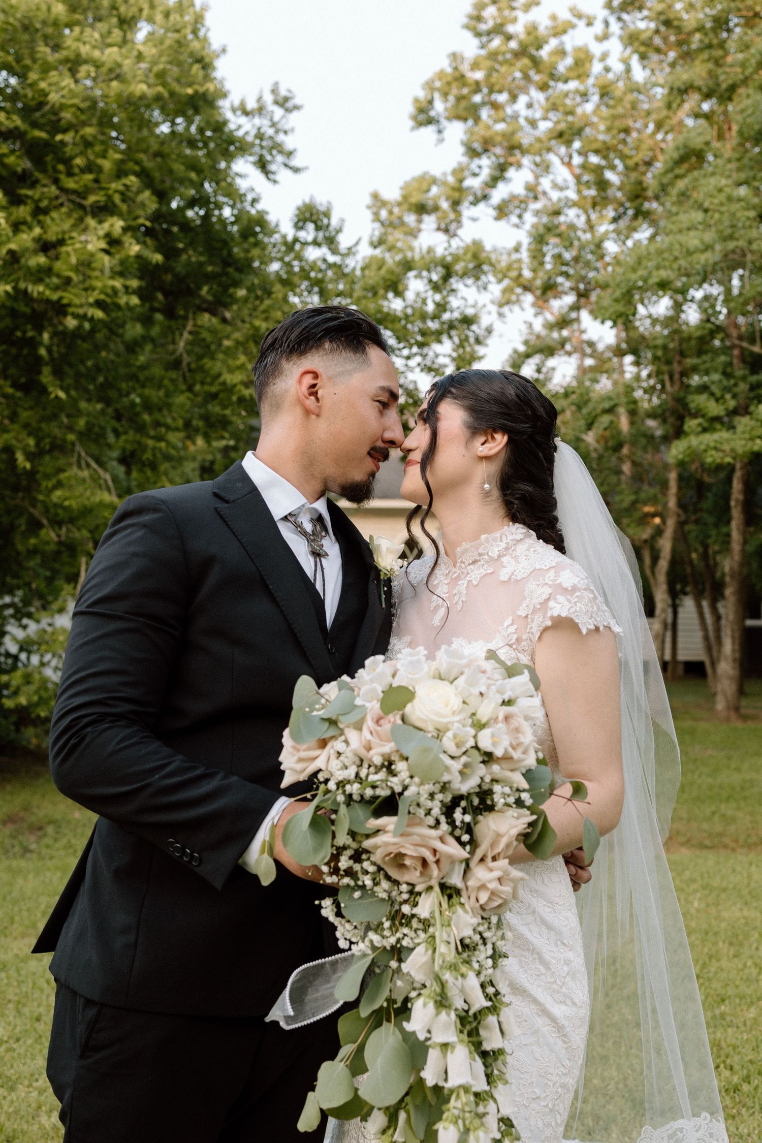Bride and groom sharing a romantic forehead touch outdoors holding a cascading floral bouquet.