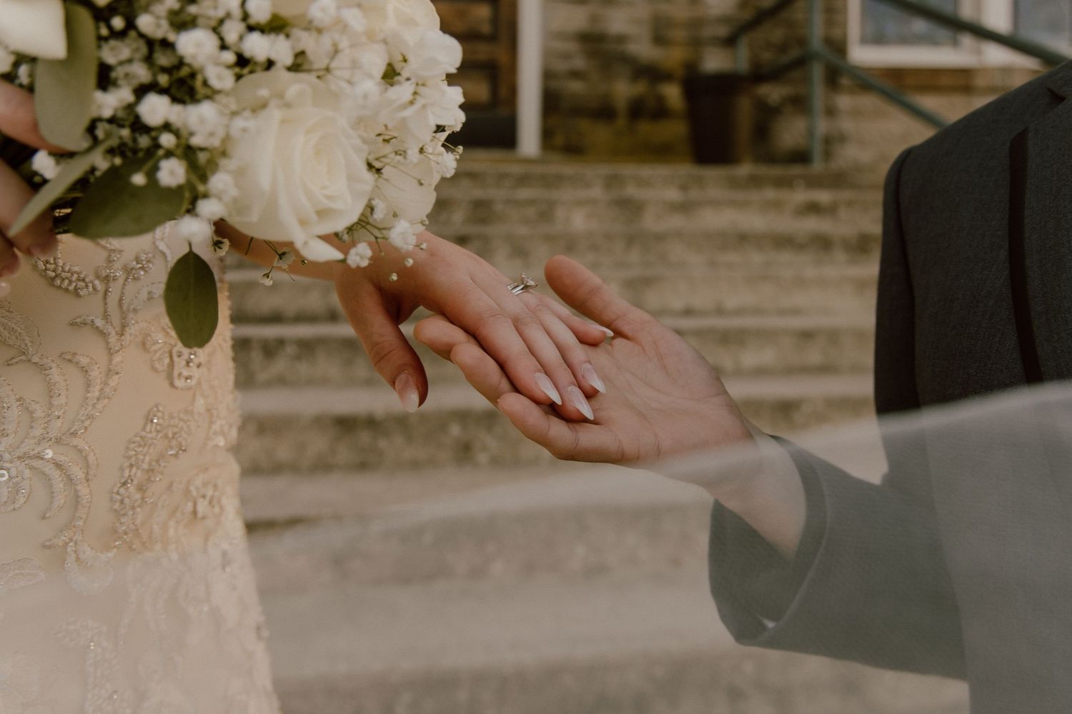 Close-up of bride and groom exchanging wedding rings with white floral bouquet in background.