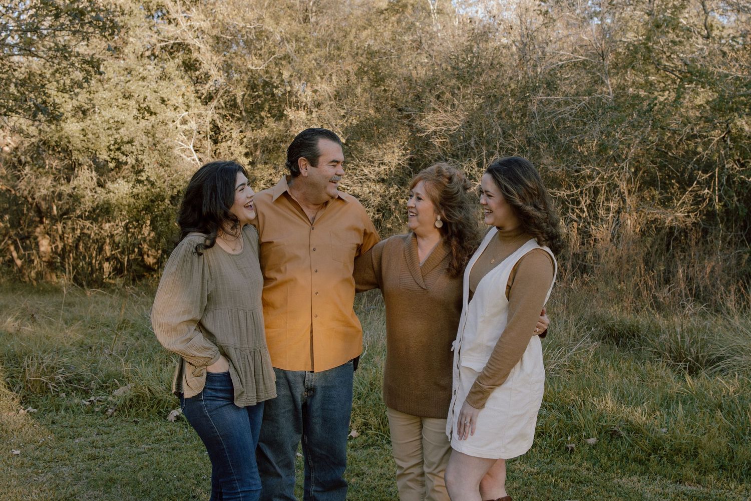 Family of four laughing and embracing together outdoors in a natural setting with autumn foliage.
