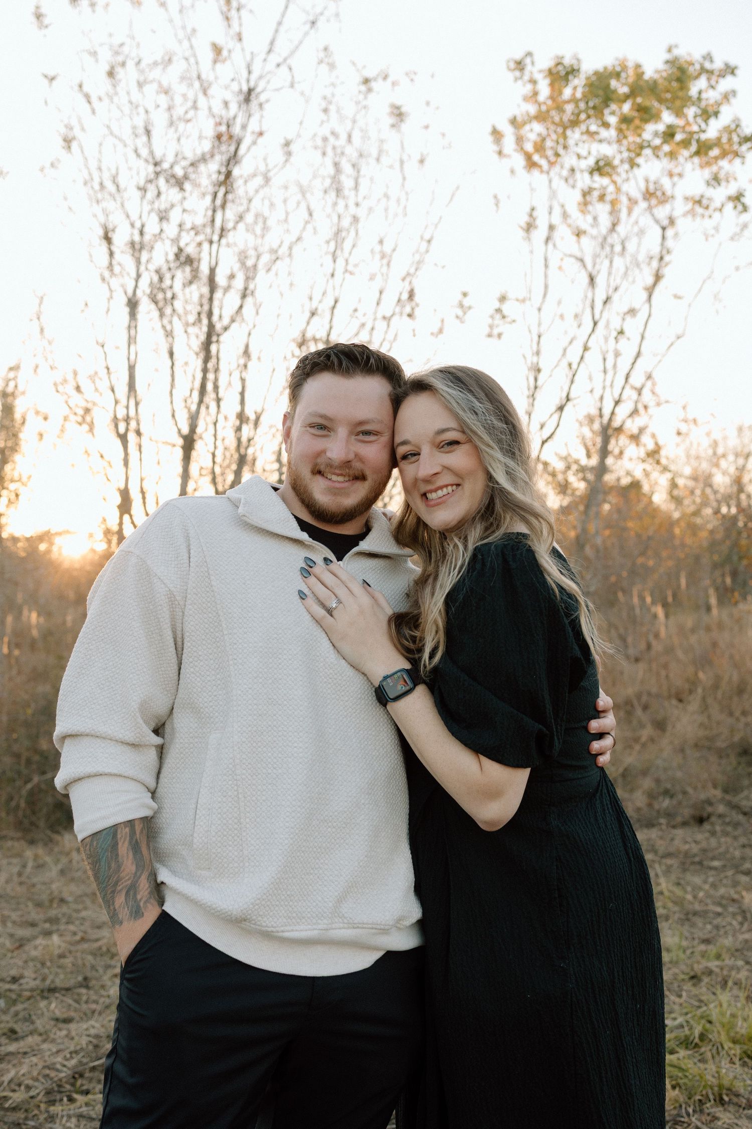 Smiling couple embraces at golden hour in a natural outdoor setting.
