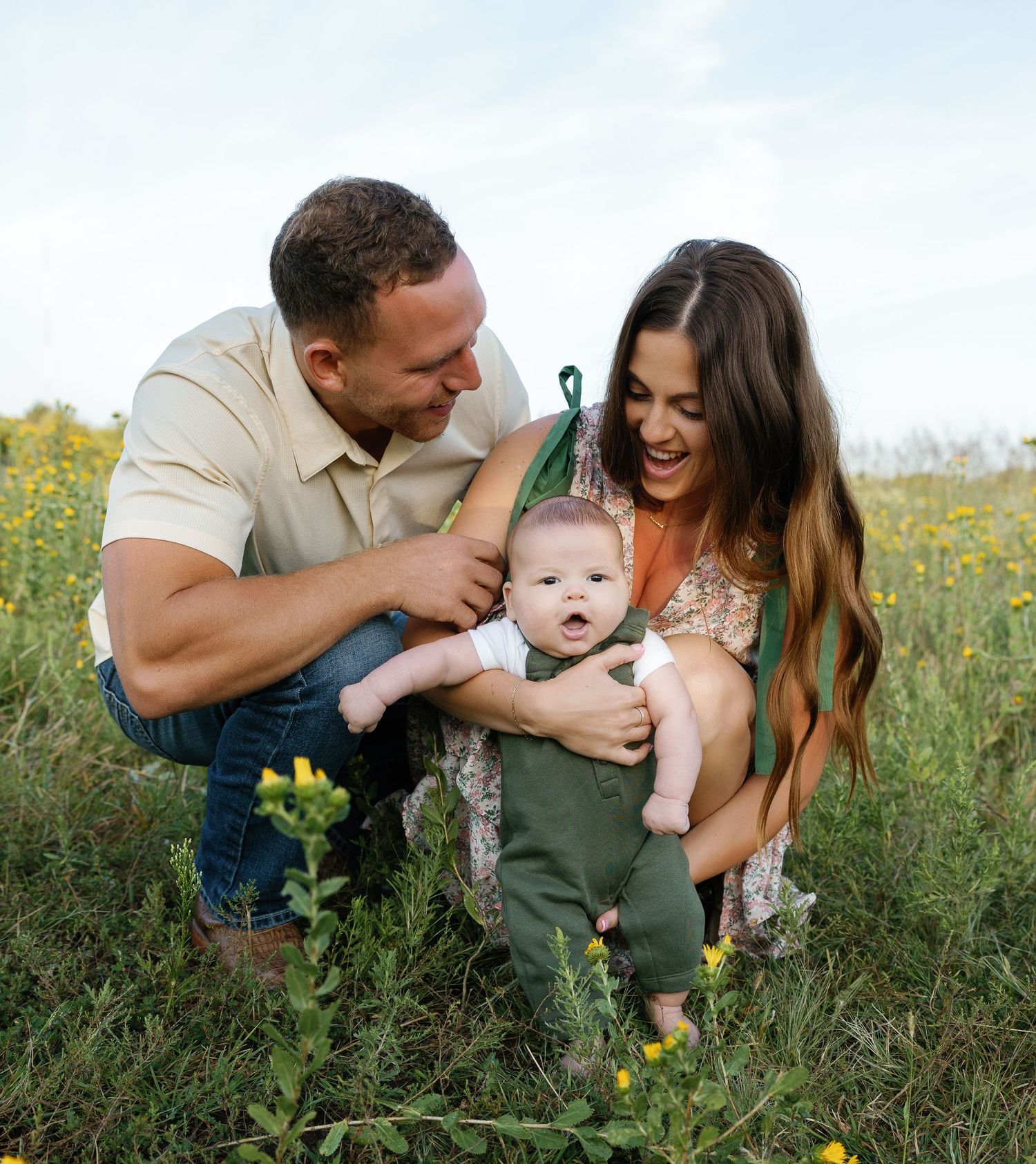 Happy young family with newborn baby laughing together in a sunny wildflower meadow.