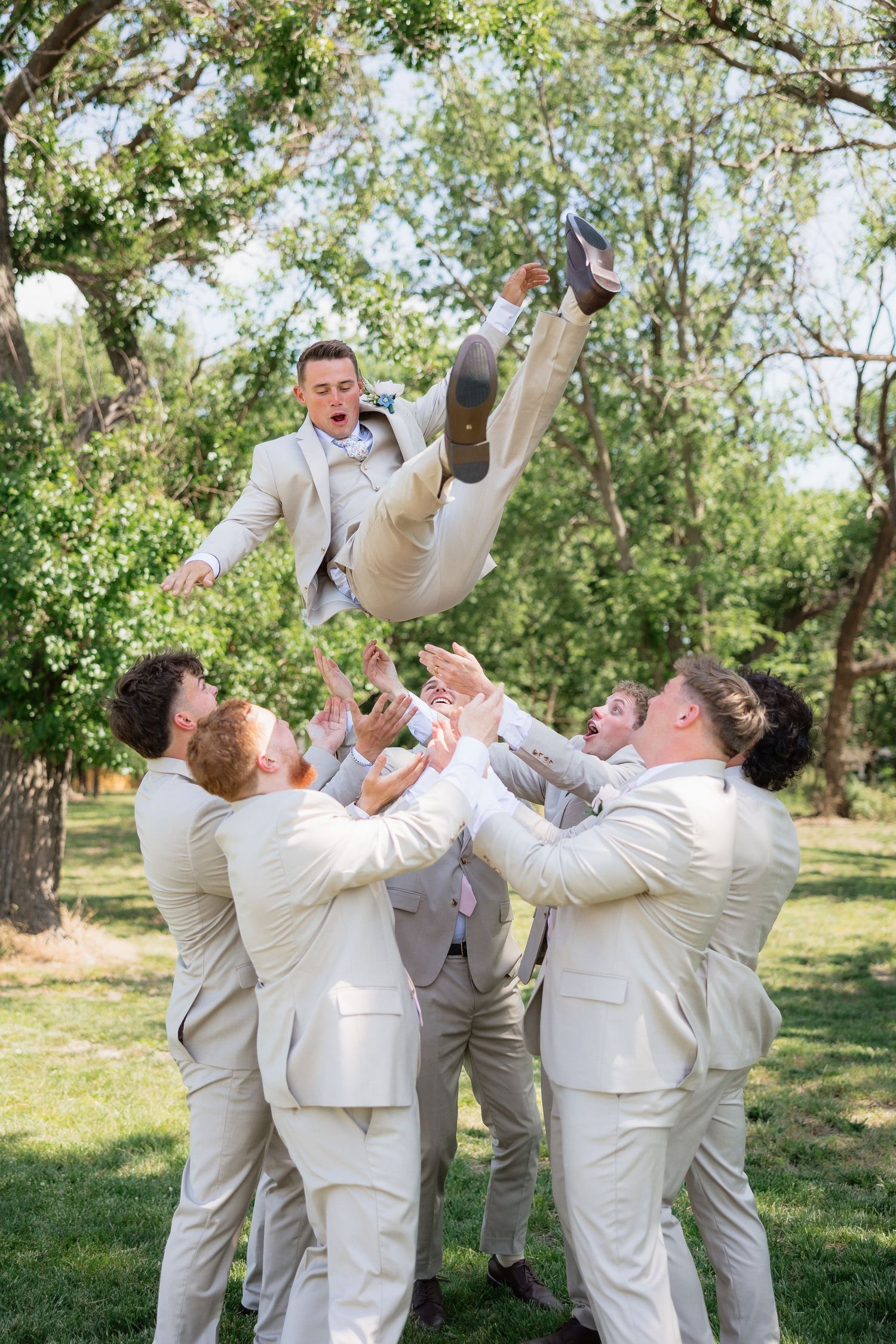 Groomsmen toss the groom into the air in a joyful outdoor celebration before the wedding ceremony.