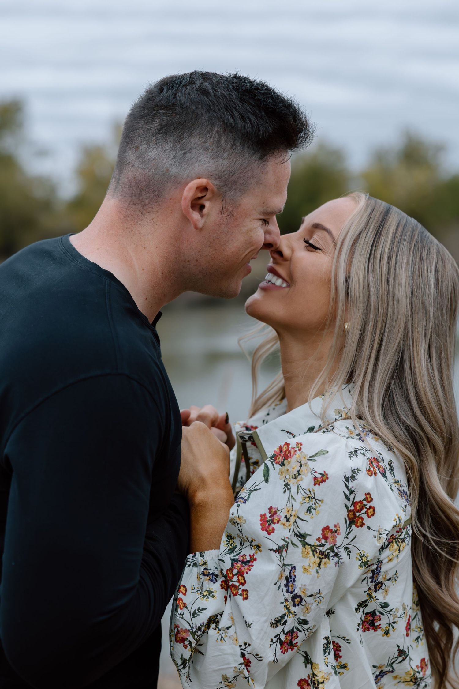 Smiling couple sharing a romantic nose-to-nose moment outdoors near a lake.