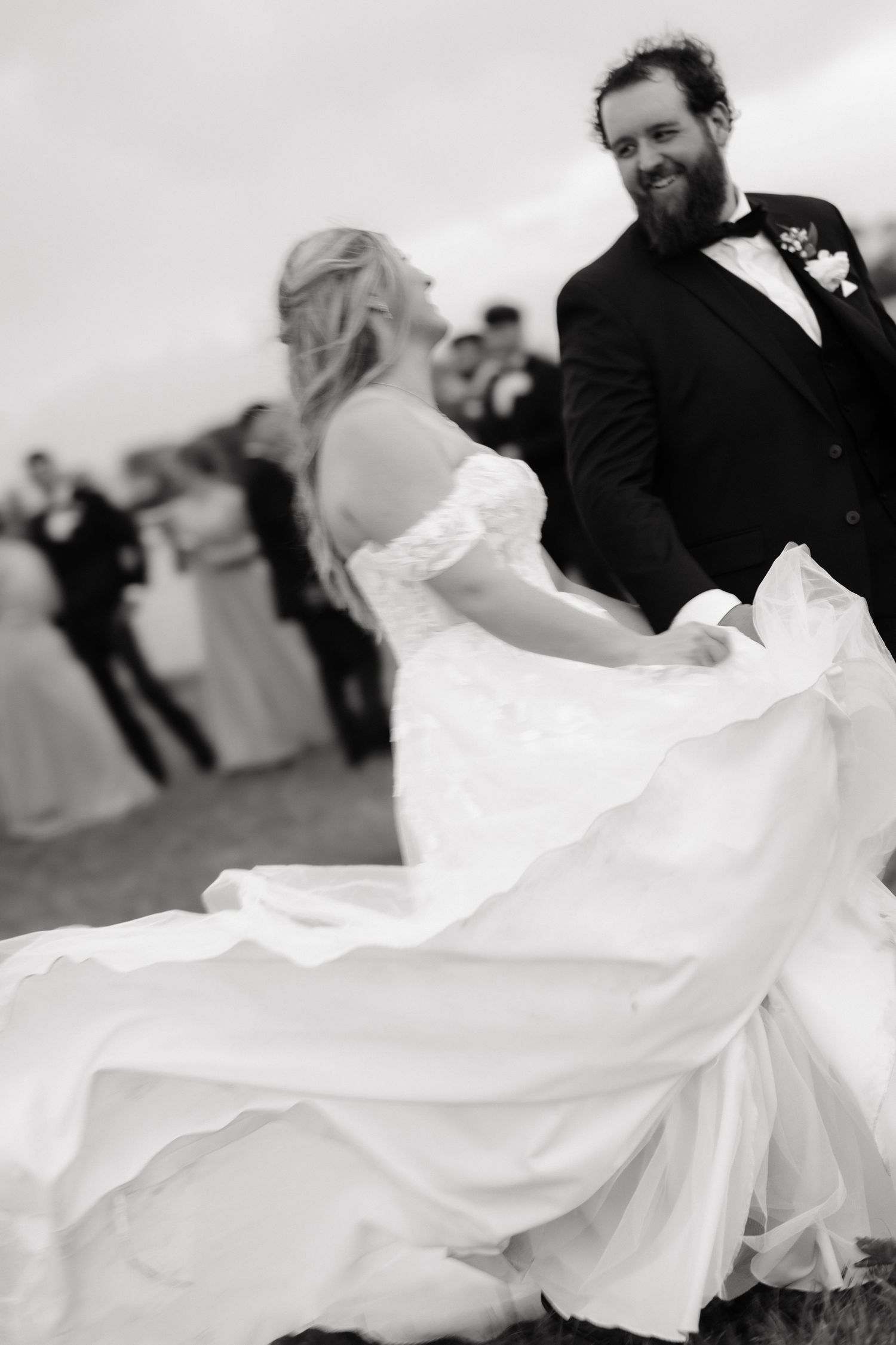 Black and white photo of smiling bearded groom watching bride twirl her flowing wedding gown.