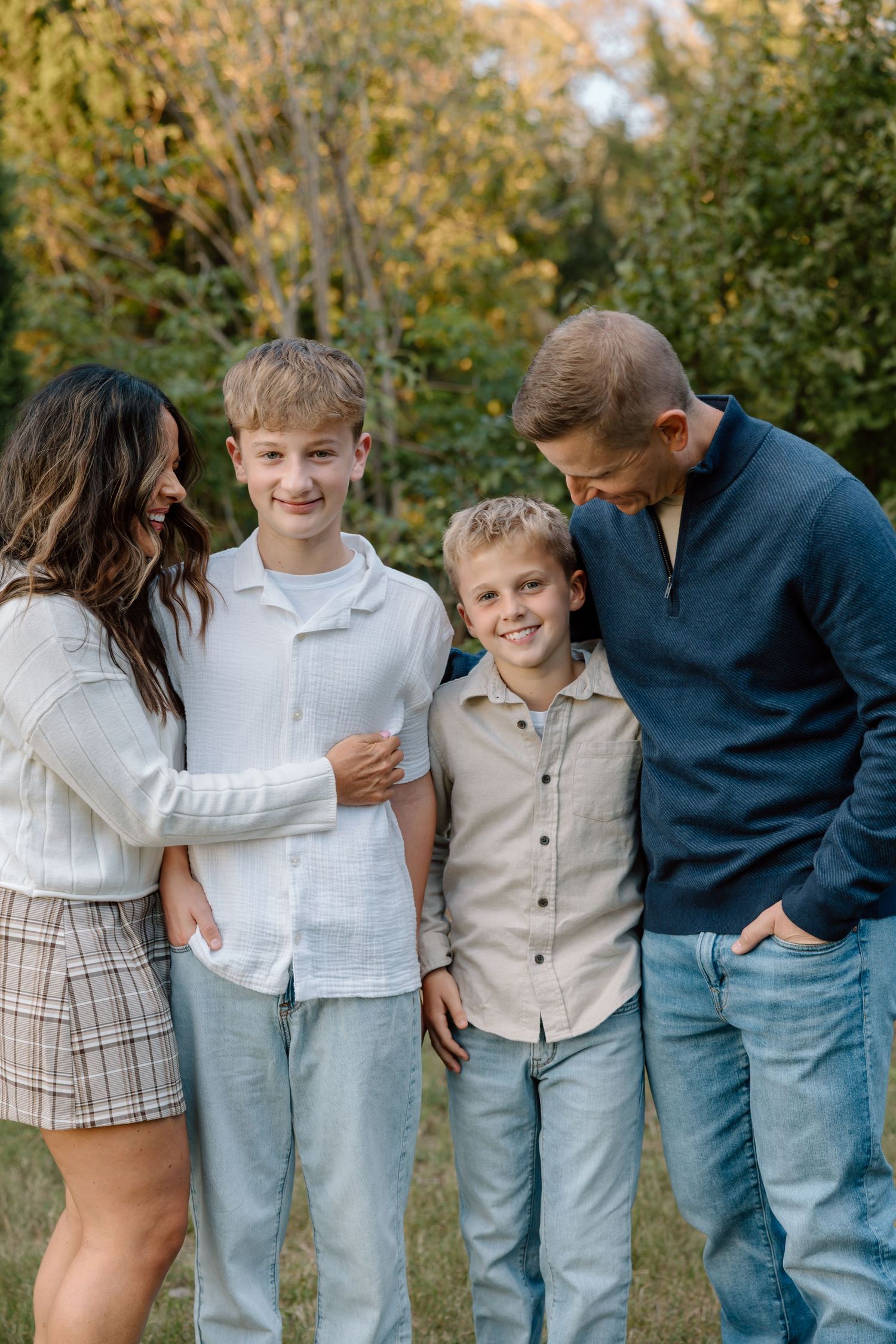Happy family of four smiling together outdoors with trees in background during fall season.