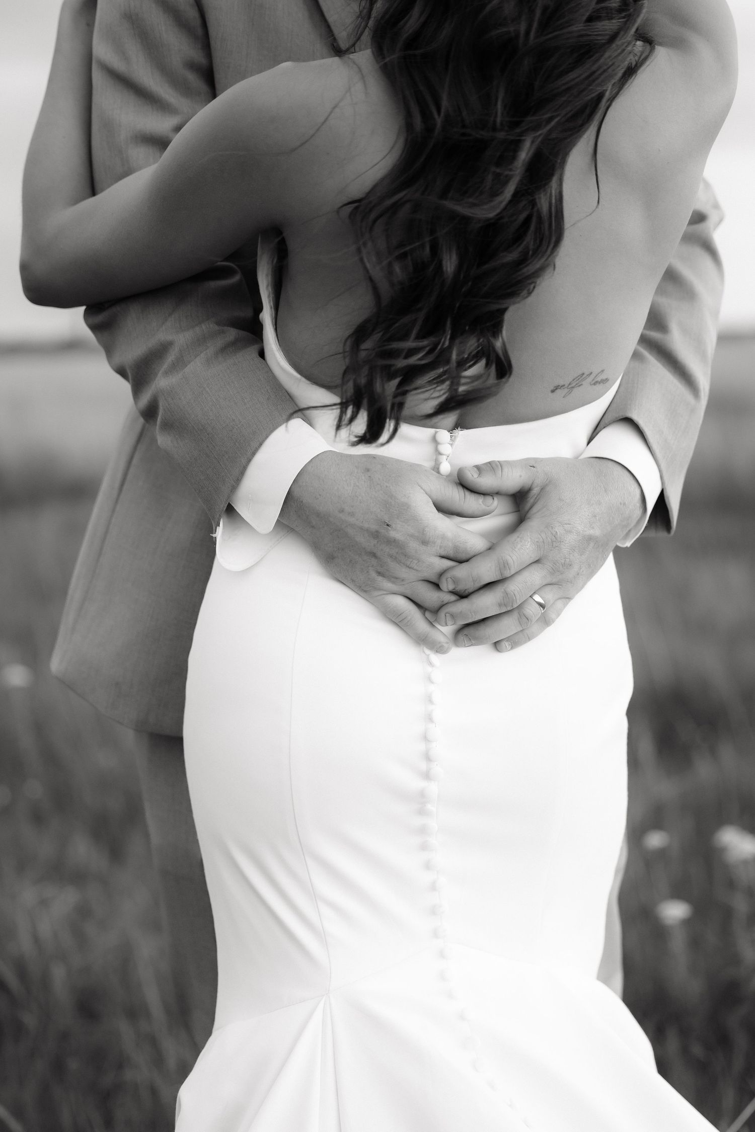 Black and white photo of groom embracing bride in fitted wedding dress with button back detail.