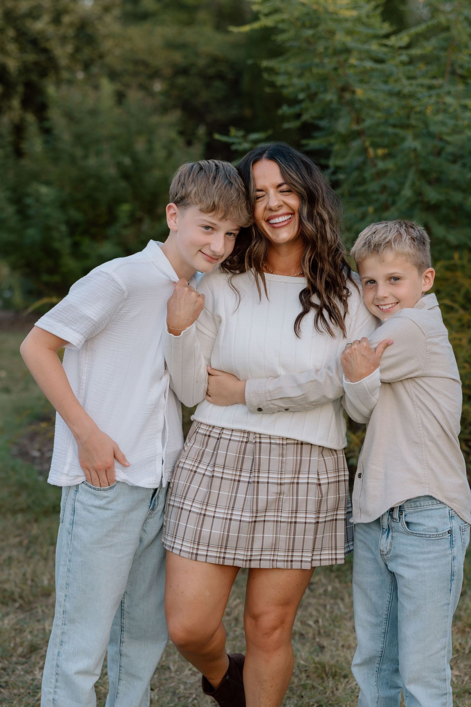Joyful mother laughing with her two young sons hugging her in an outdoor setting.