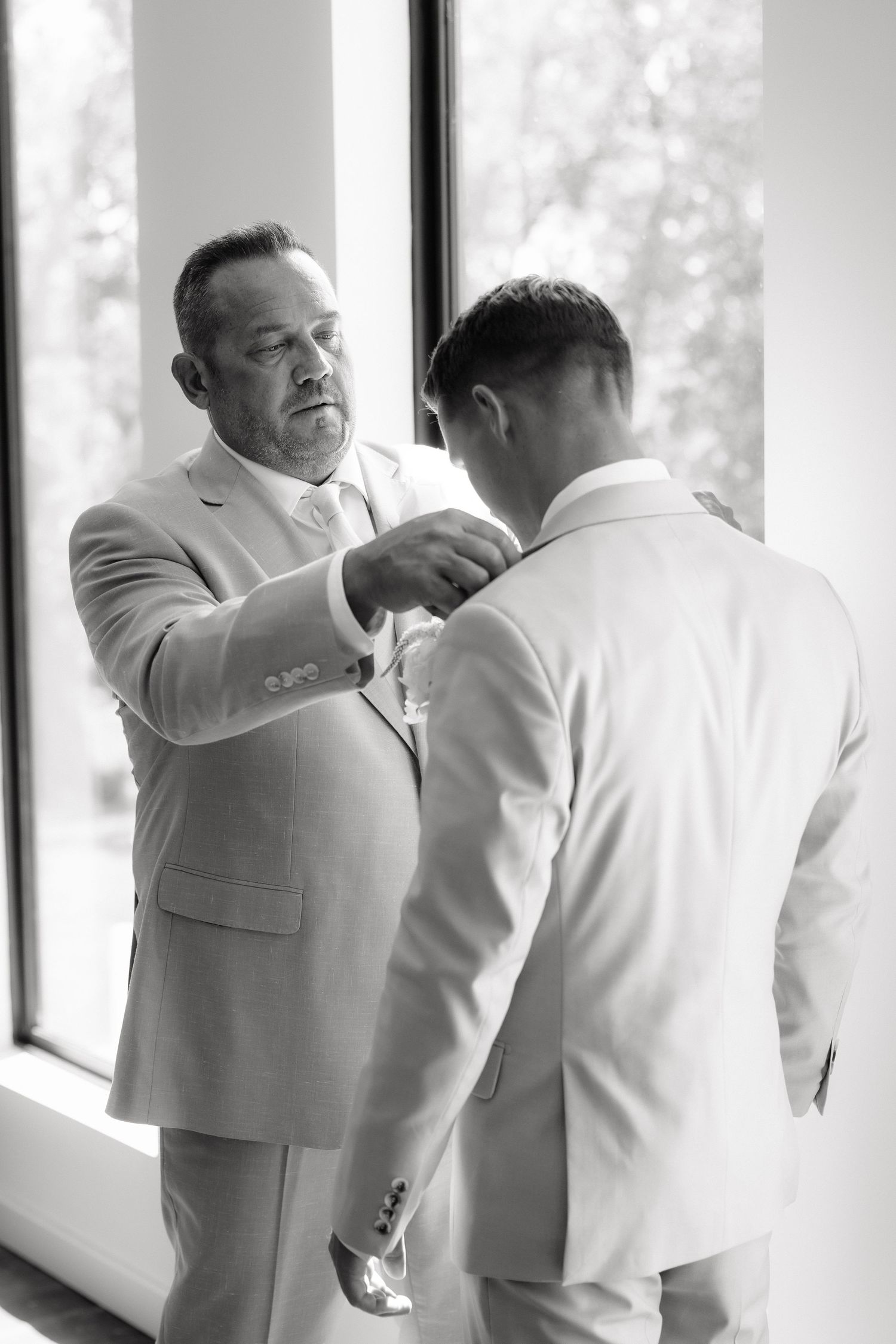 Black and white photo of a father helping his son adjust his suit jacket before the wedding ceremony.